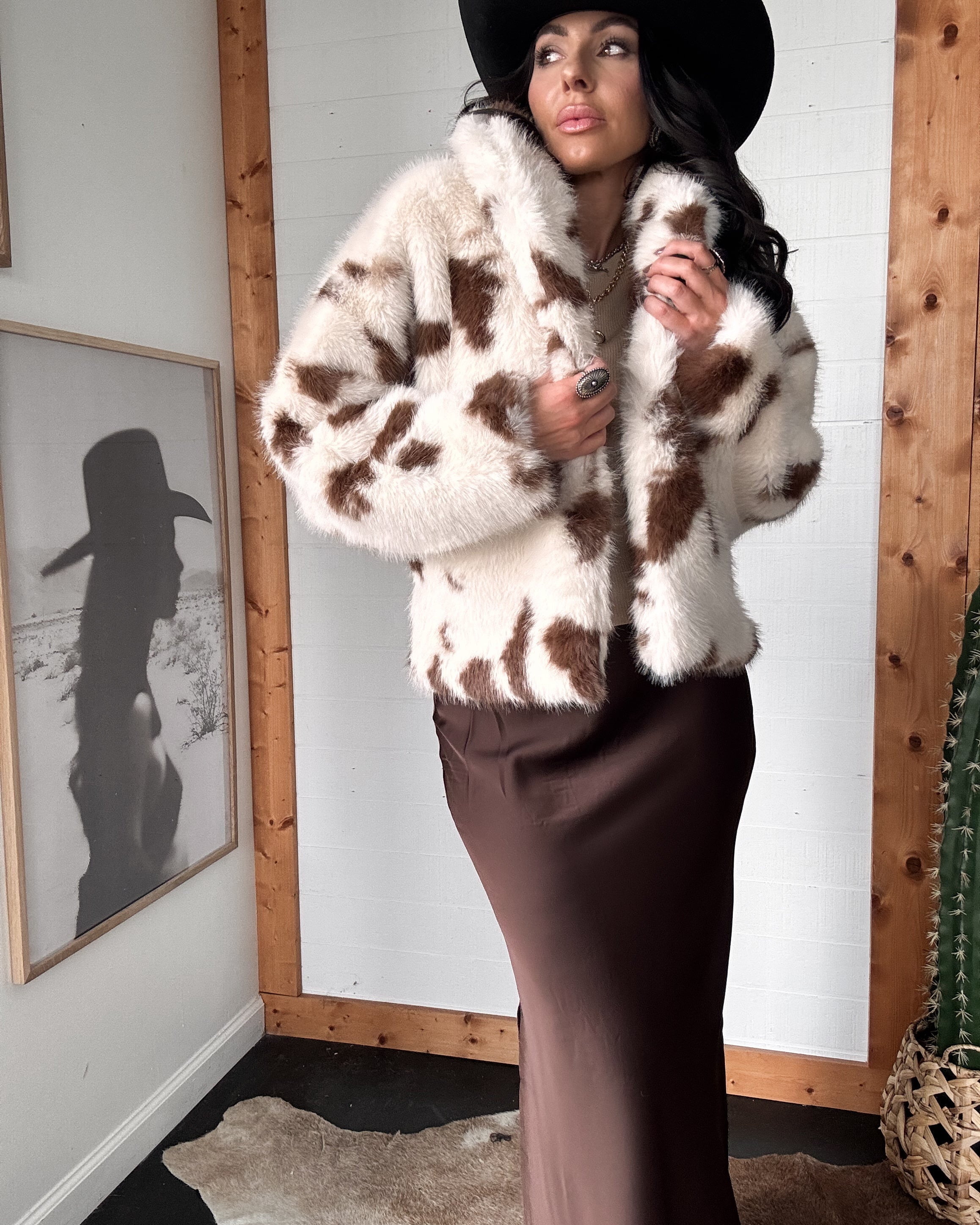 Woman wearing a cow print fur coat and black hat indoors.