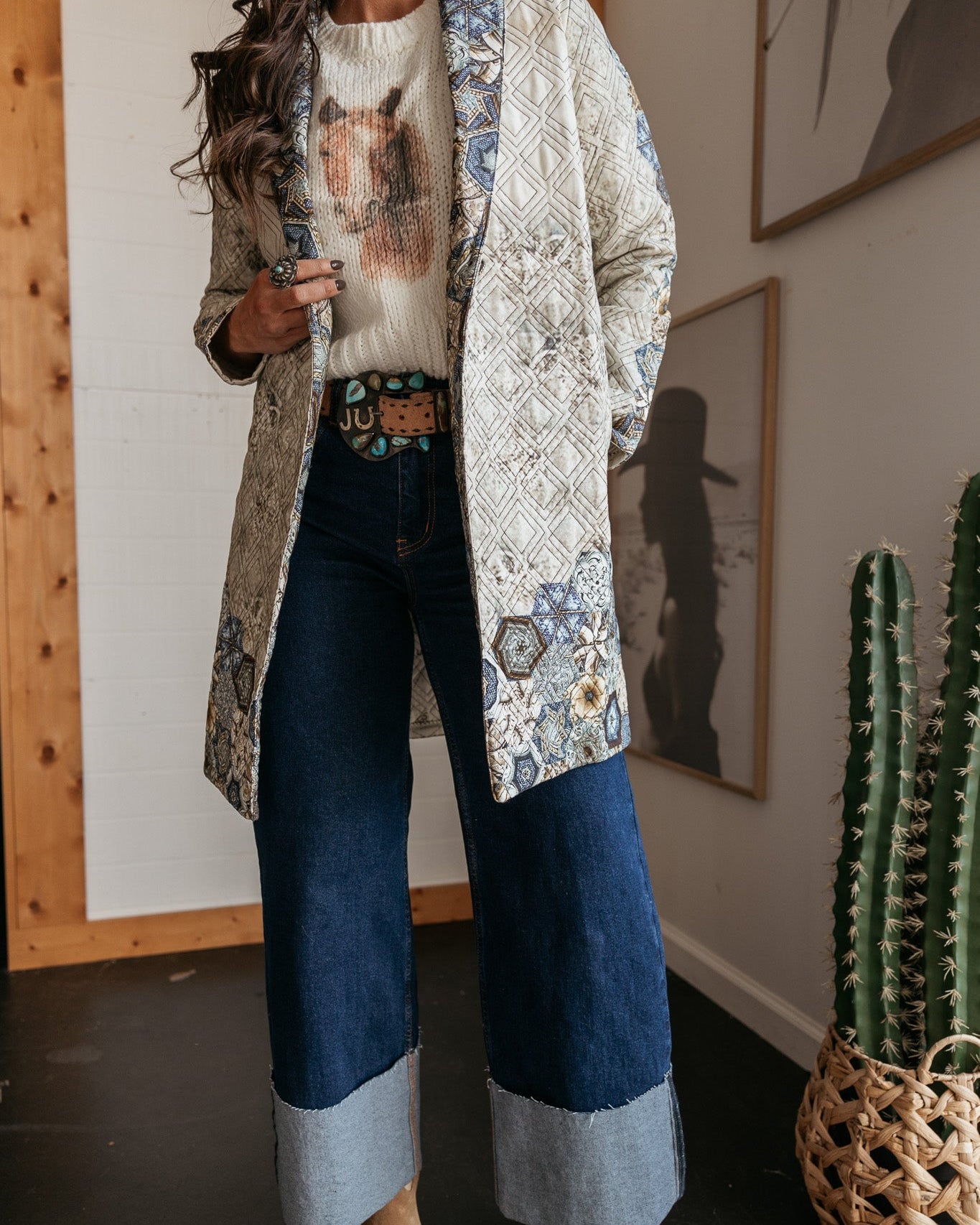 Woman in western boho outfit with patterned quilted jacket, horse sweater, wide leg jeans, and cowboy boots
