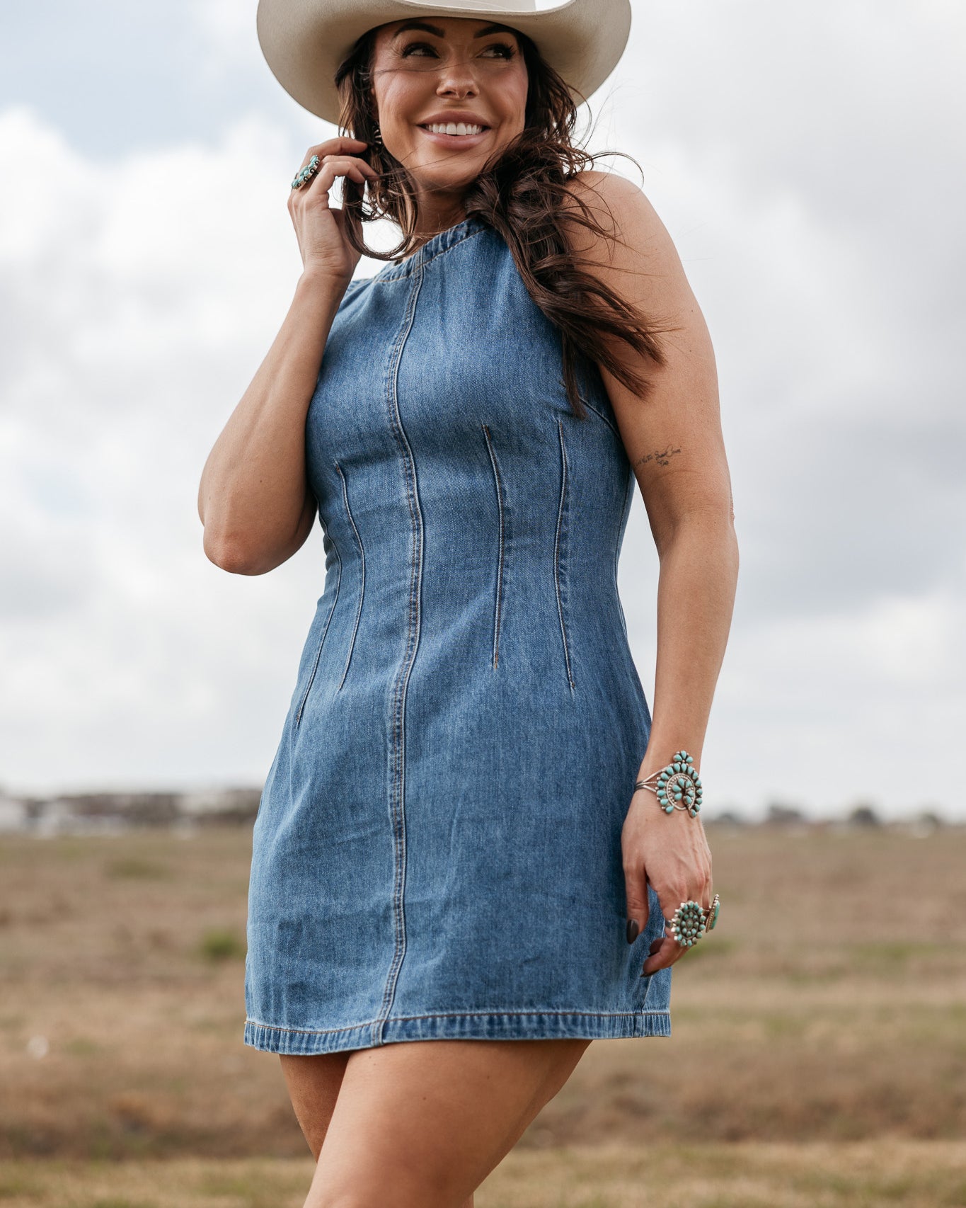 Woman in denim western dress, ivory cowboy hat, turquoise jewelry, standing outdoors