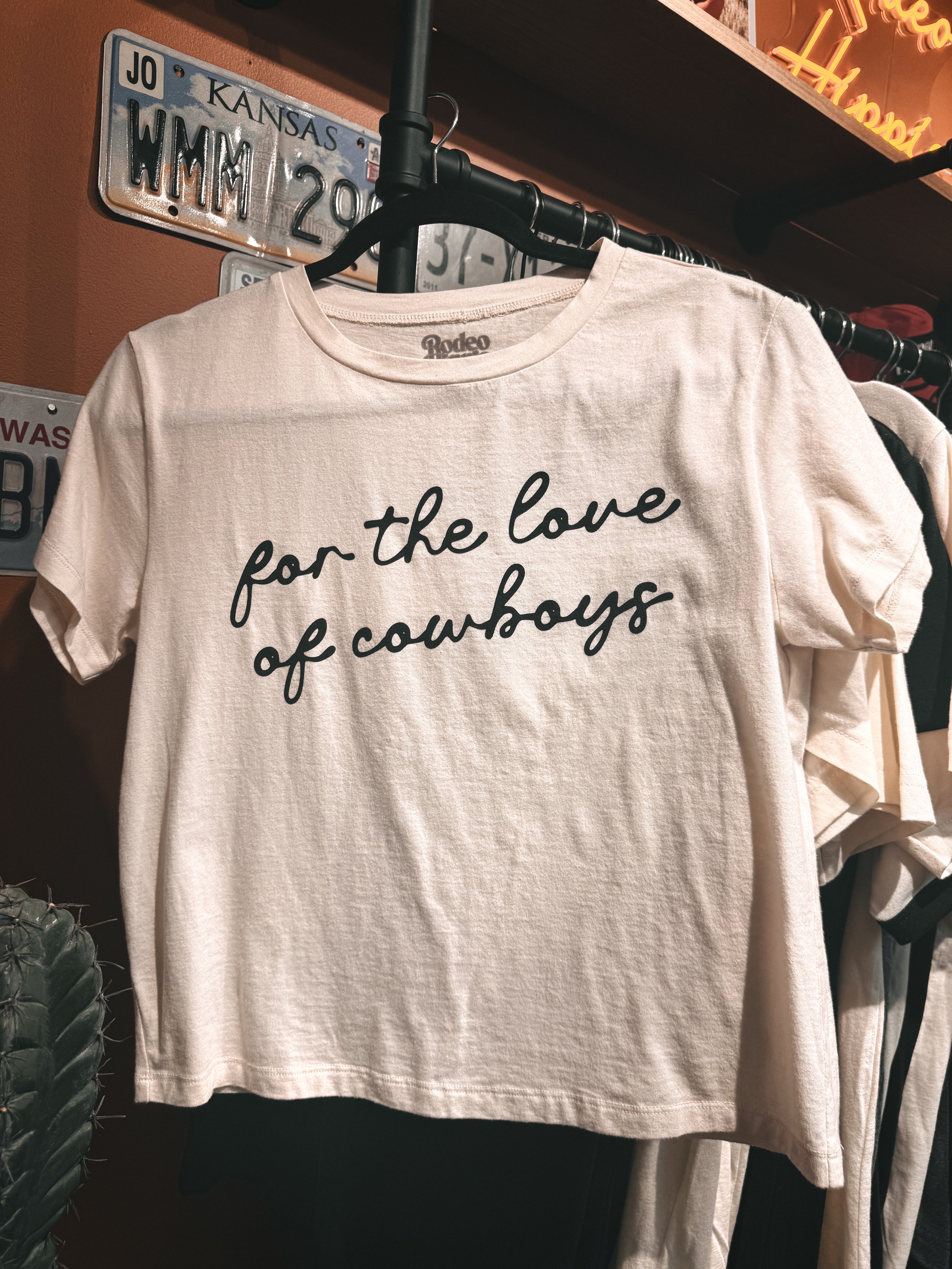 Beige t-shirt with 'For the love of cowboys' text on a hanger.