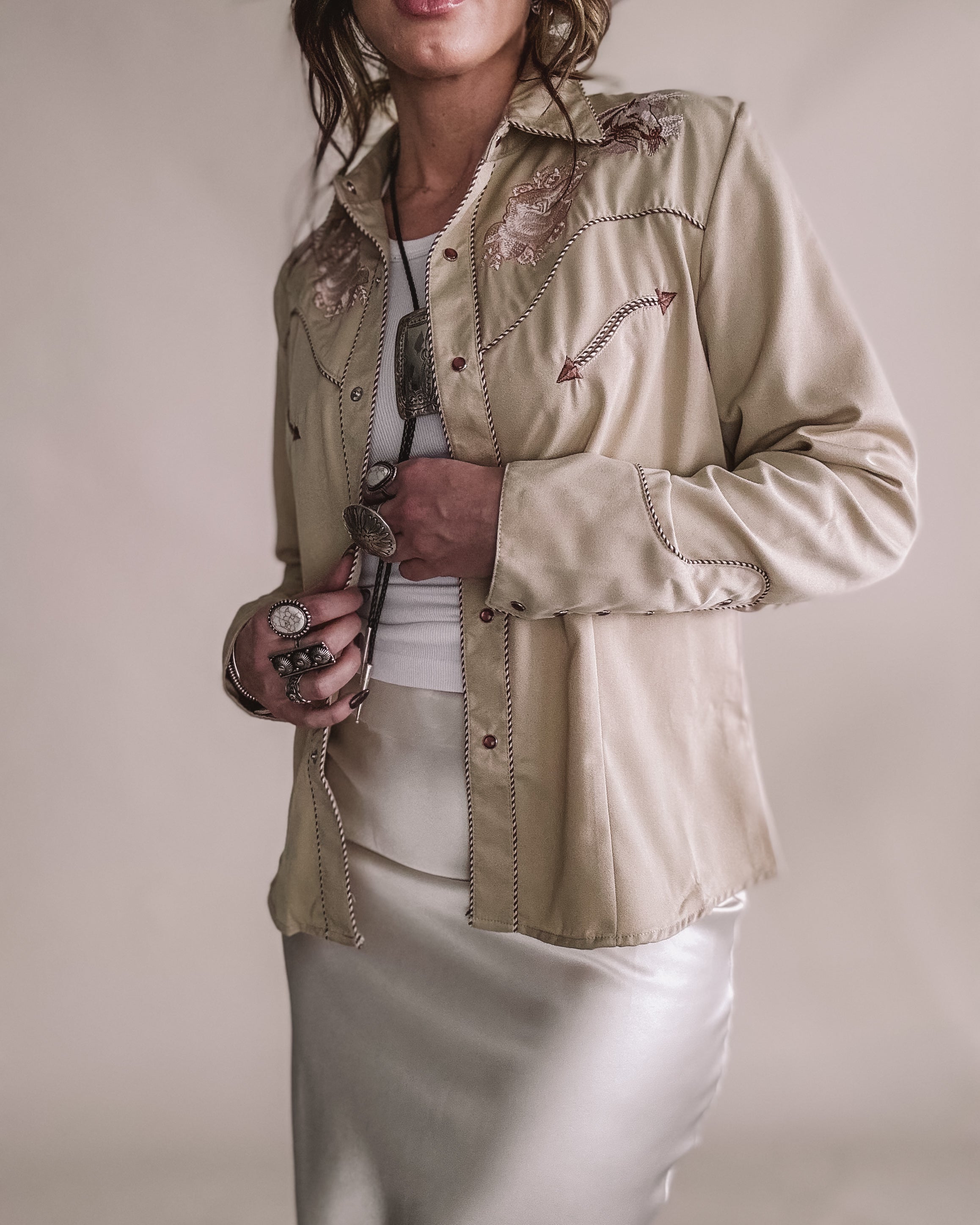 Woman in embroidered western shirt, satin skirt, cowgirl hat, and boho jewelry