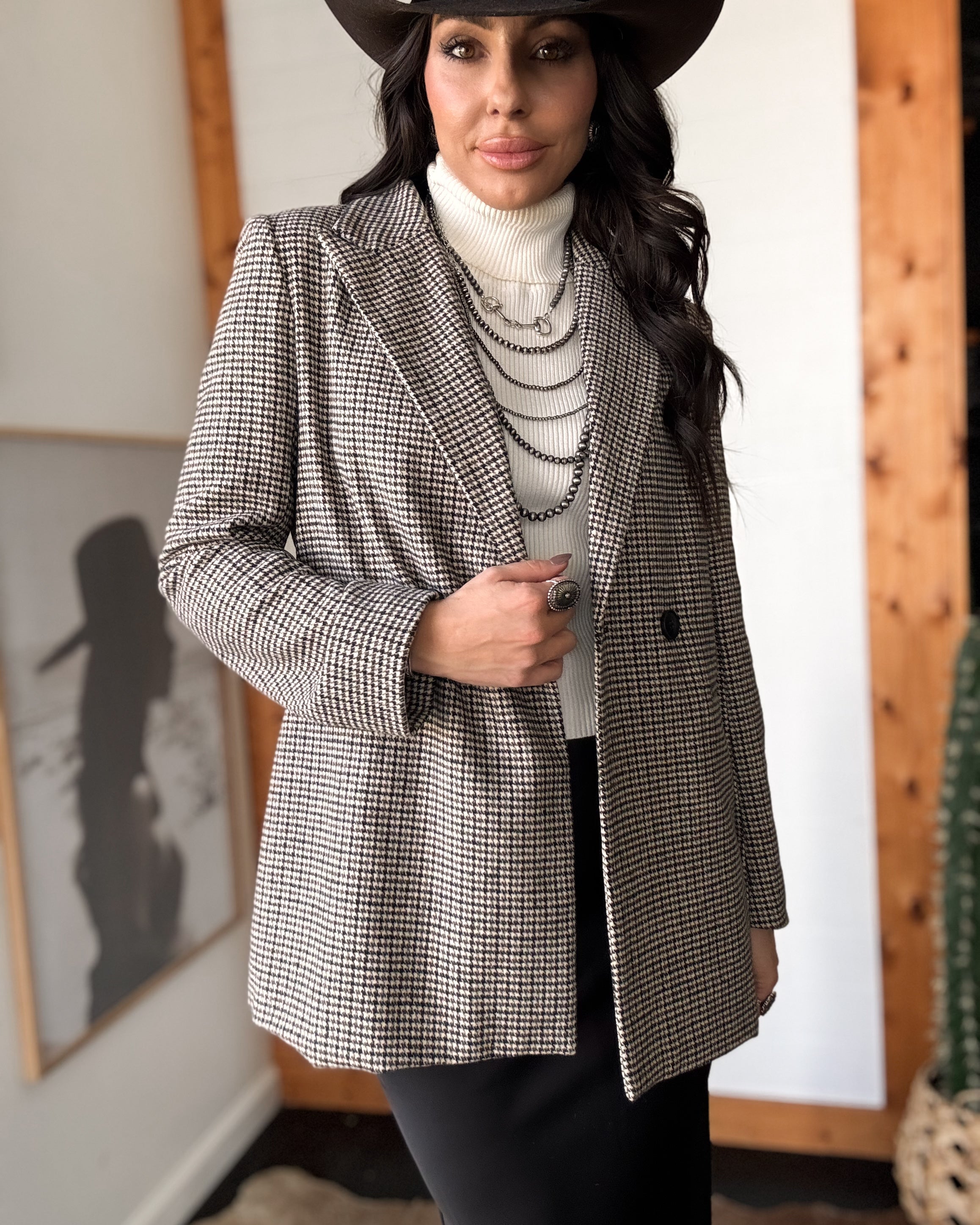 Woman in western boho outfit with houndstooth blazer, white turtleneck, black hat, layered necklaces