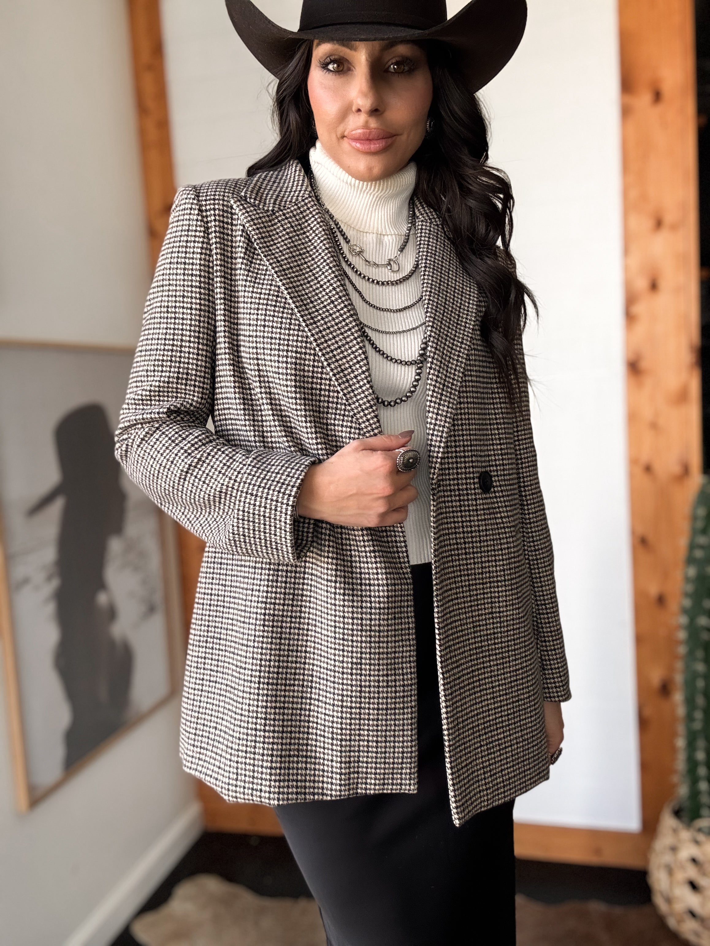 Woman in western boho outfit with houndstooth blazer, white turtleneck, black hat, layered necklaces