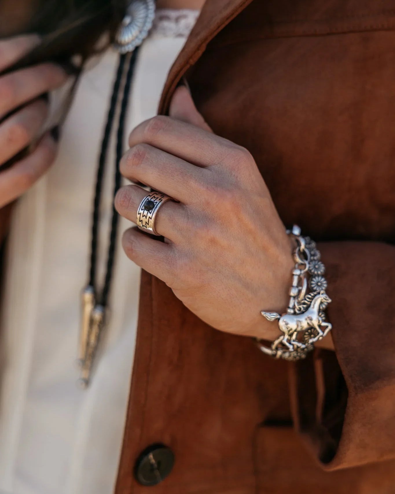 Woman wearing western boho jewelry, silver horse bracelet, concho ring, suede jacket.
