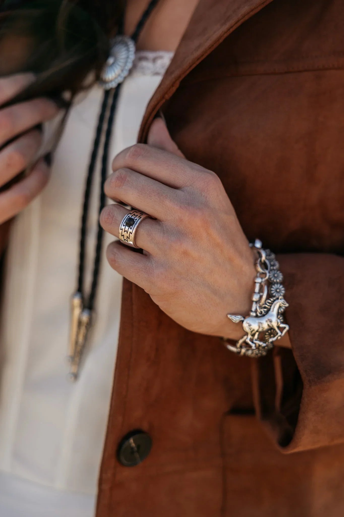 Woman wearing western boho jewelry, silver horse bracelet, concho ring, suede jacket.