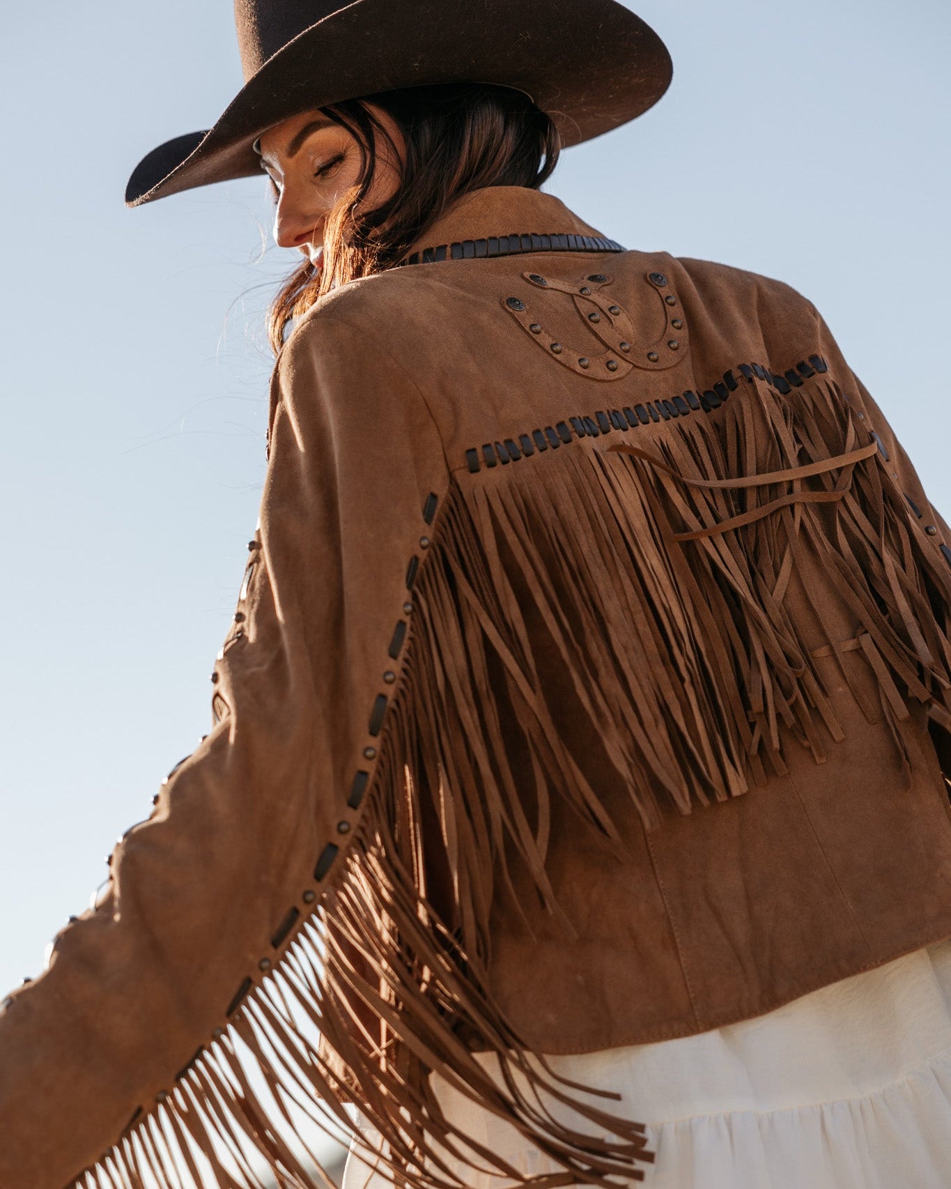 Woman in brown suede fringe western jacket and black cowboy hat, boho cowgirl style