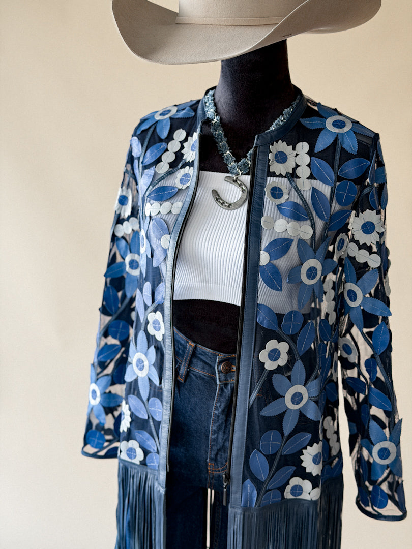 Western boho outfit with blue floral fringe jacket, white crop top, jeans, and cowboy hat