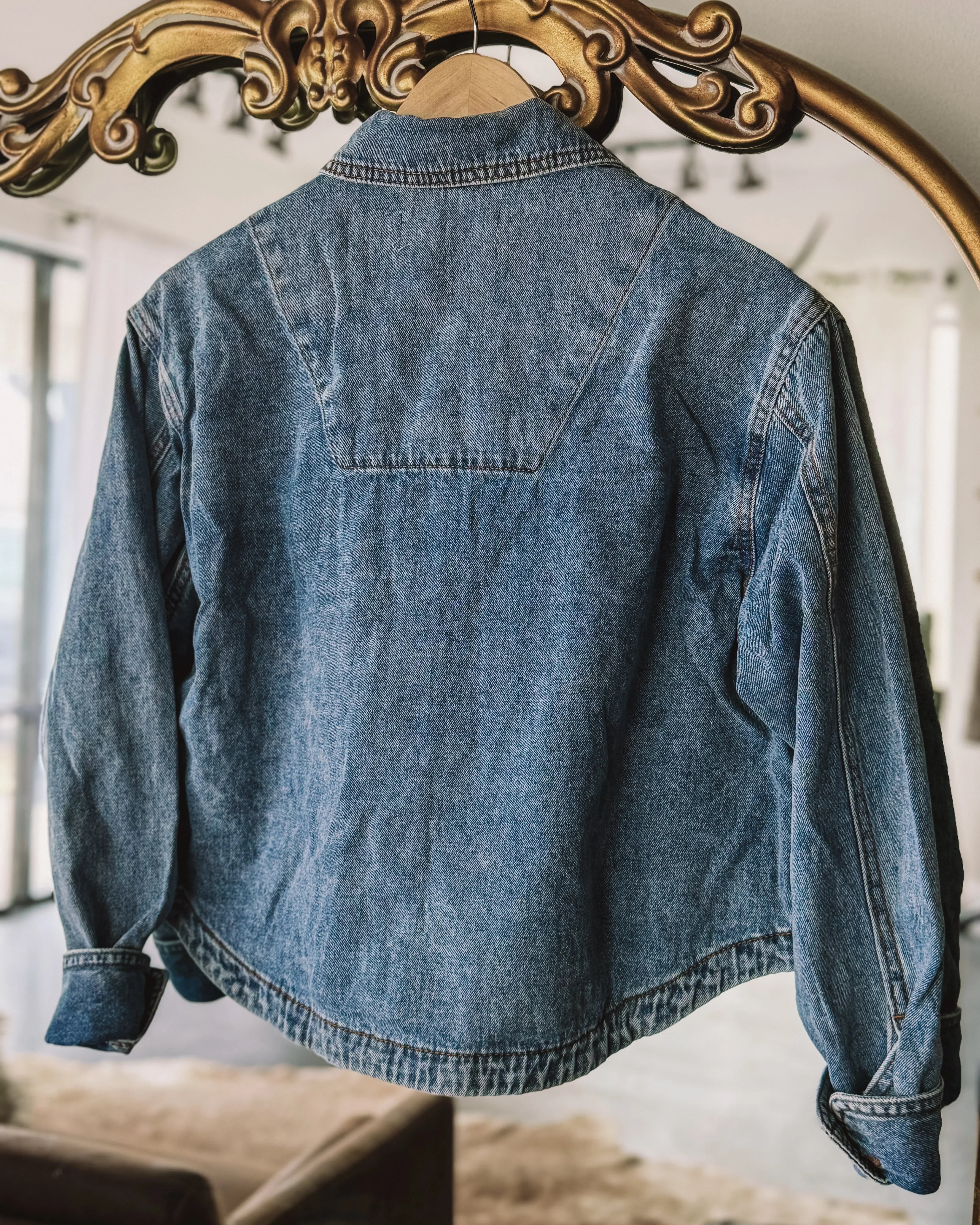 Vintage blue denim jacket with western yoke detail hanging on ornate mirror