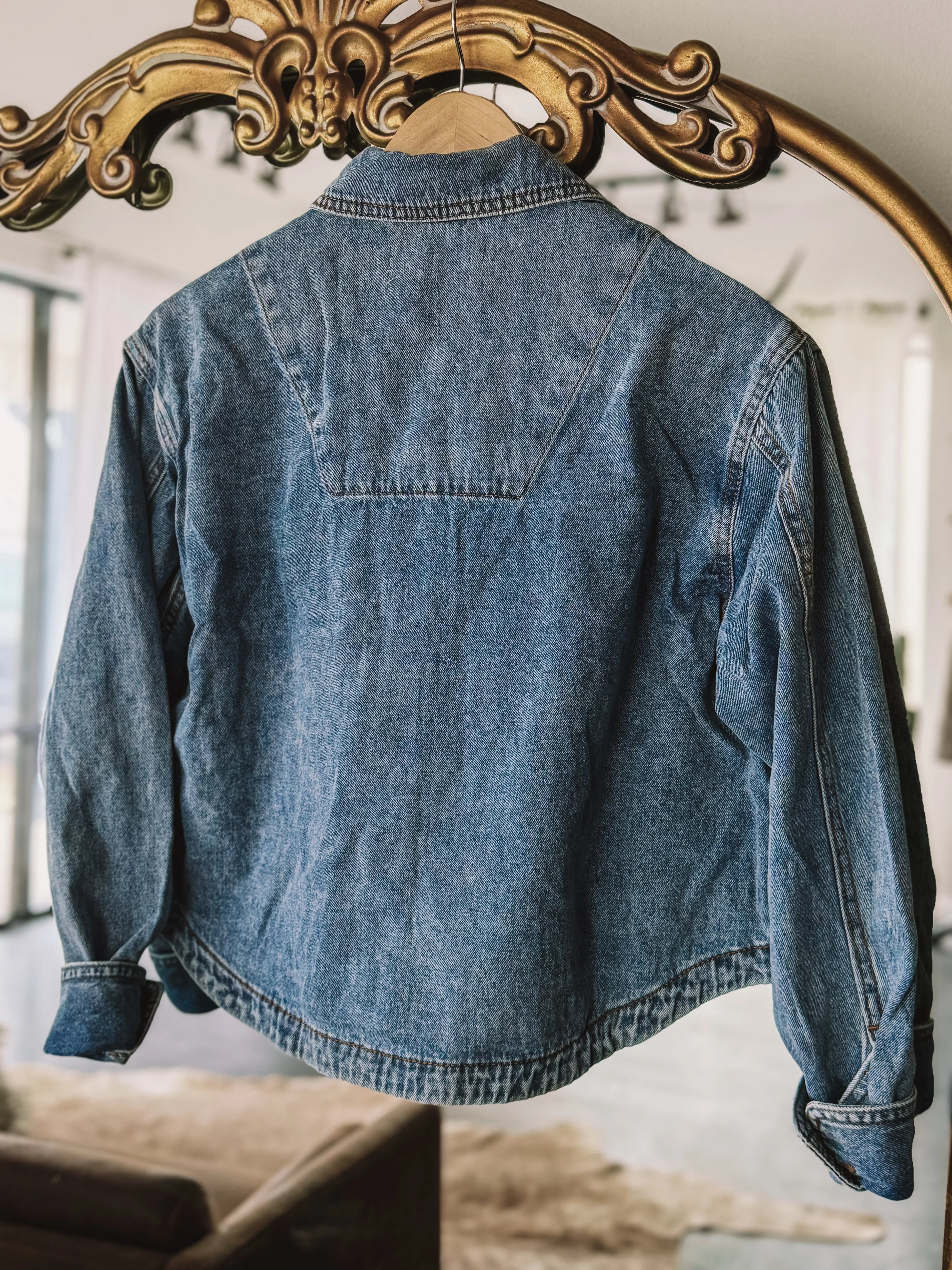 Vintage blue denim jacket with western yoke detail hanging on ornate mirror