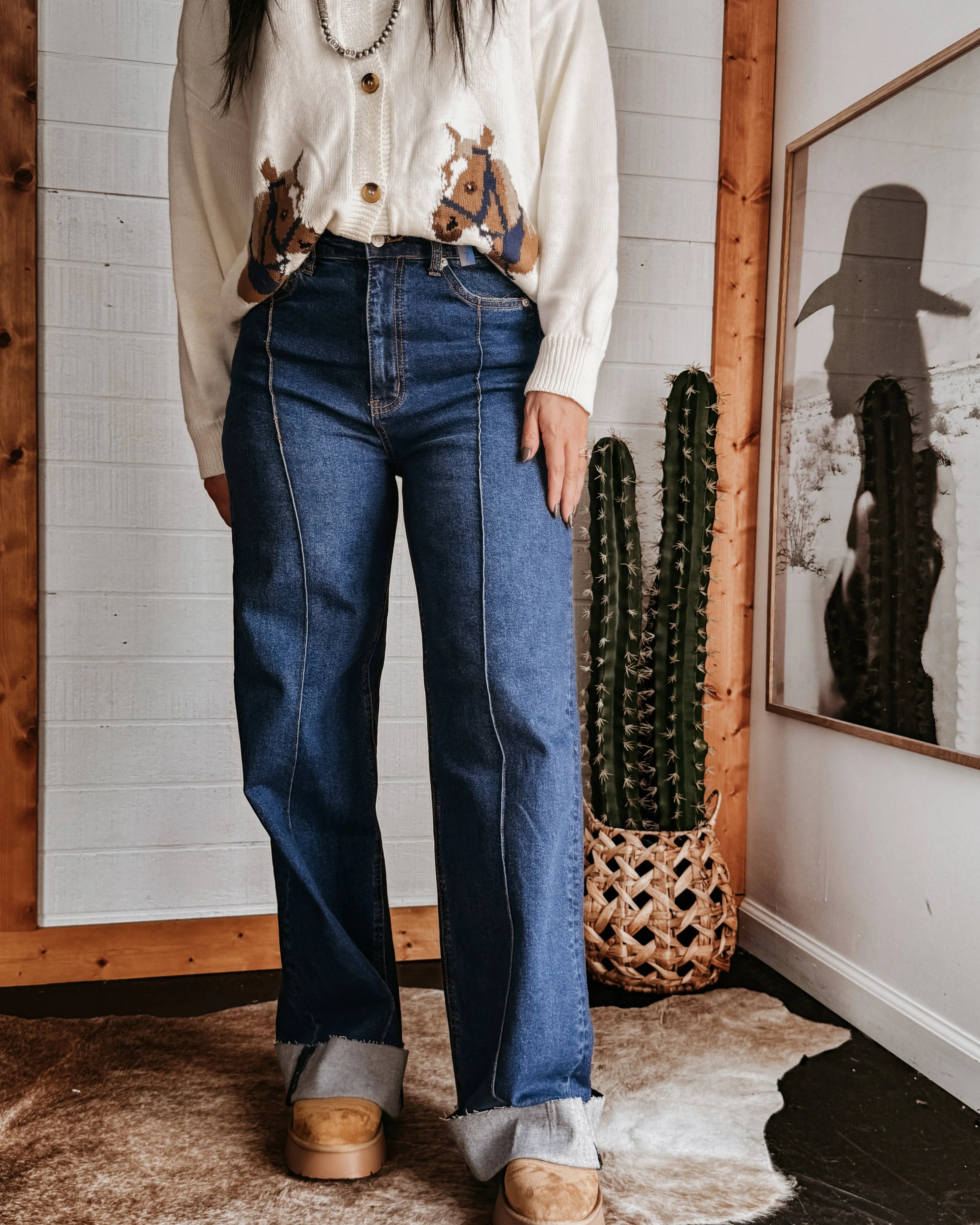 Woman wearing western boho jeans, horse print cardigan, and boots, styled with a cactus decor.