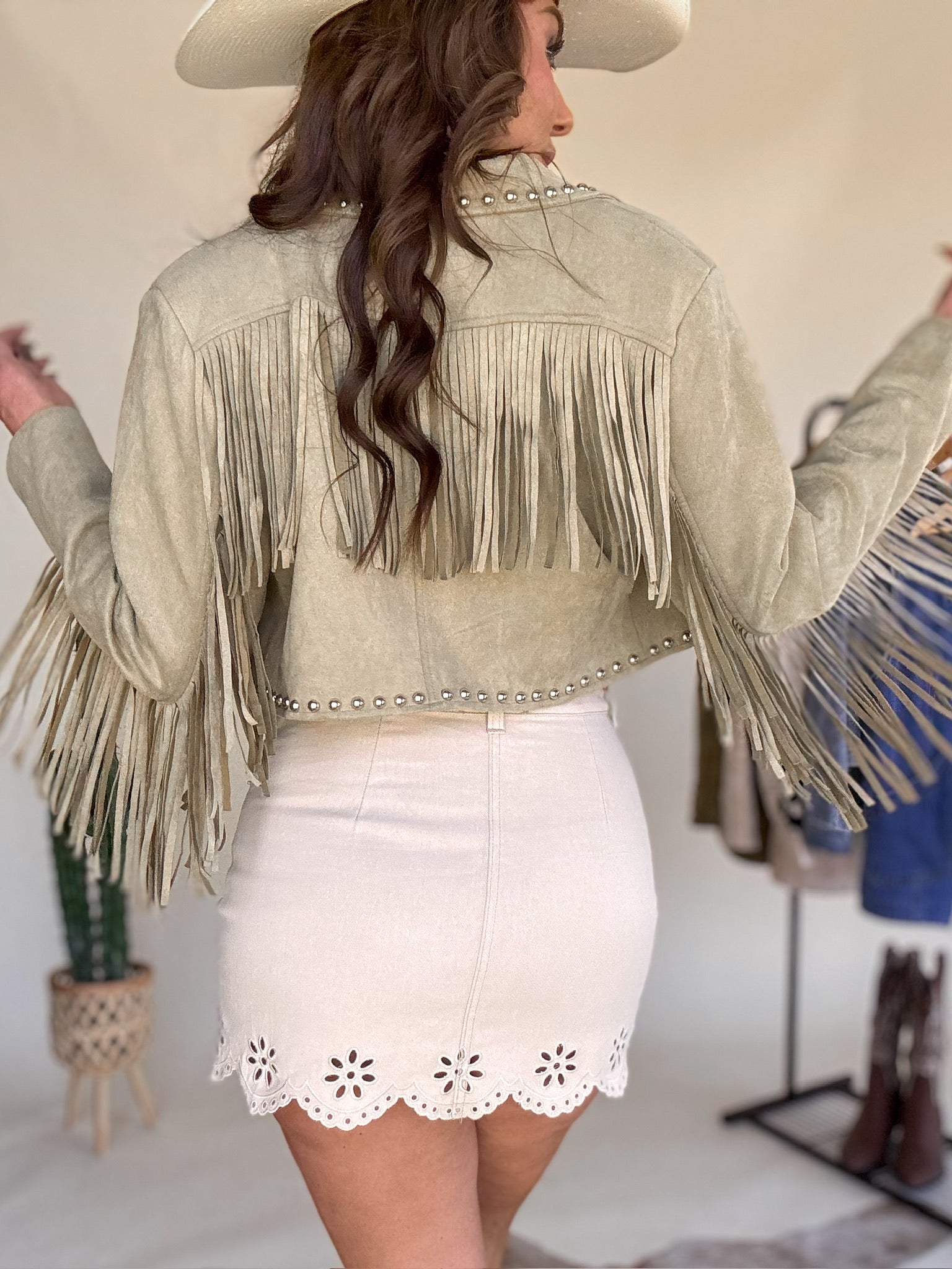 Woman in western boho outfit, tan fringe jacket, white eyelet mini skirt, and cowboy hat
