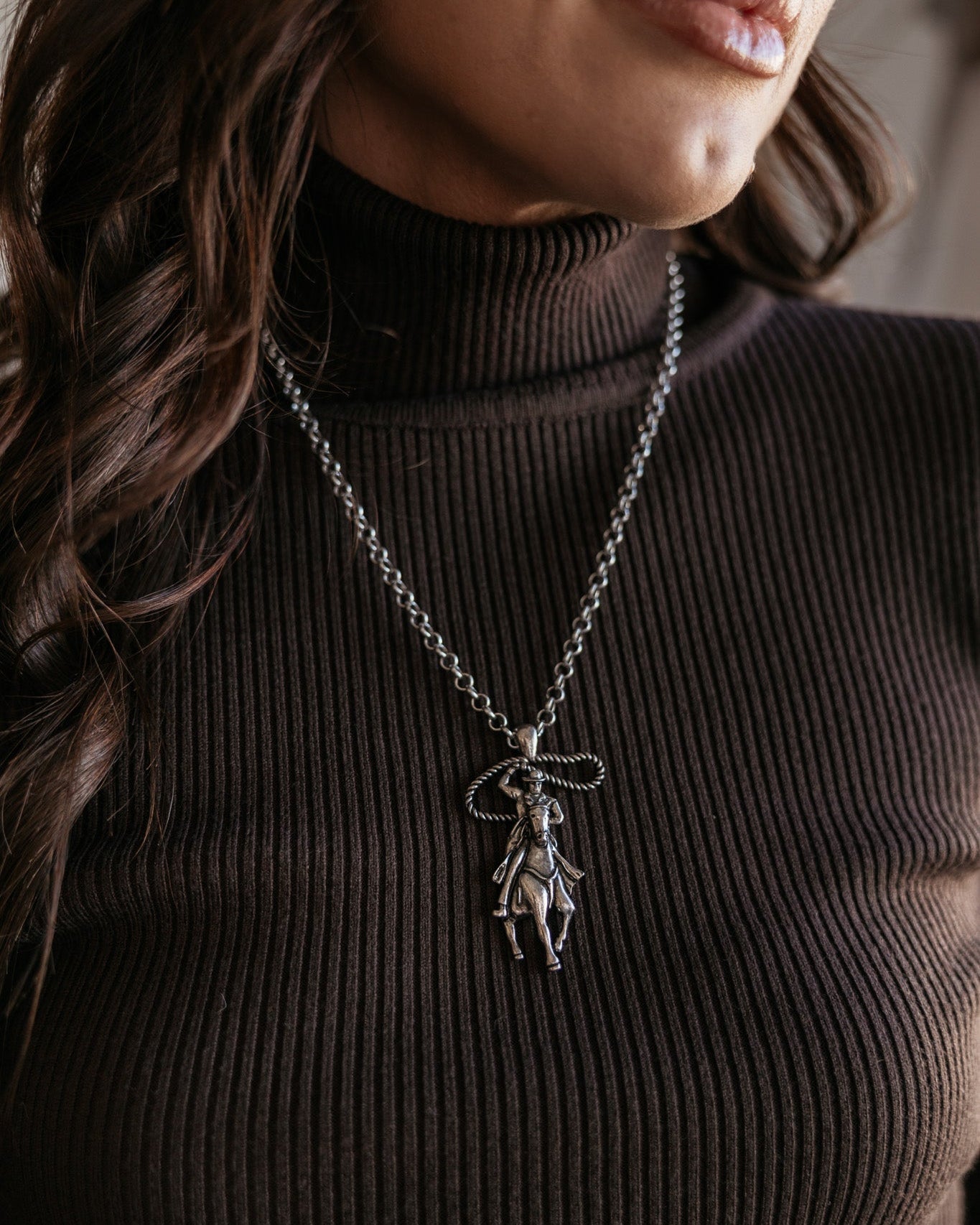 Woman wearing western cowgirl necklace with horse pendant over ribbed brown turtleneck top