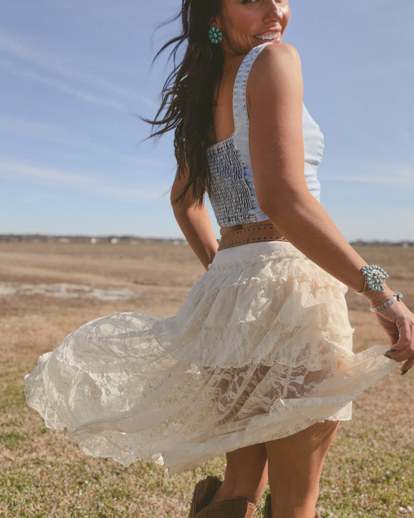 Woman in lace western skirt, blue crop top, turquoise jewelry, and cowboy boots outdoors