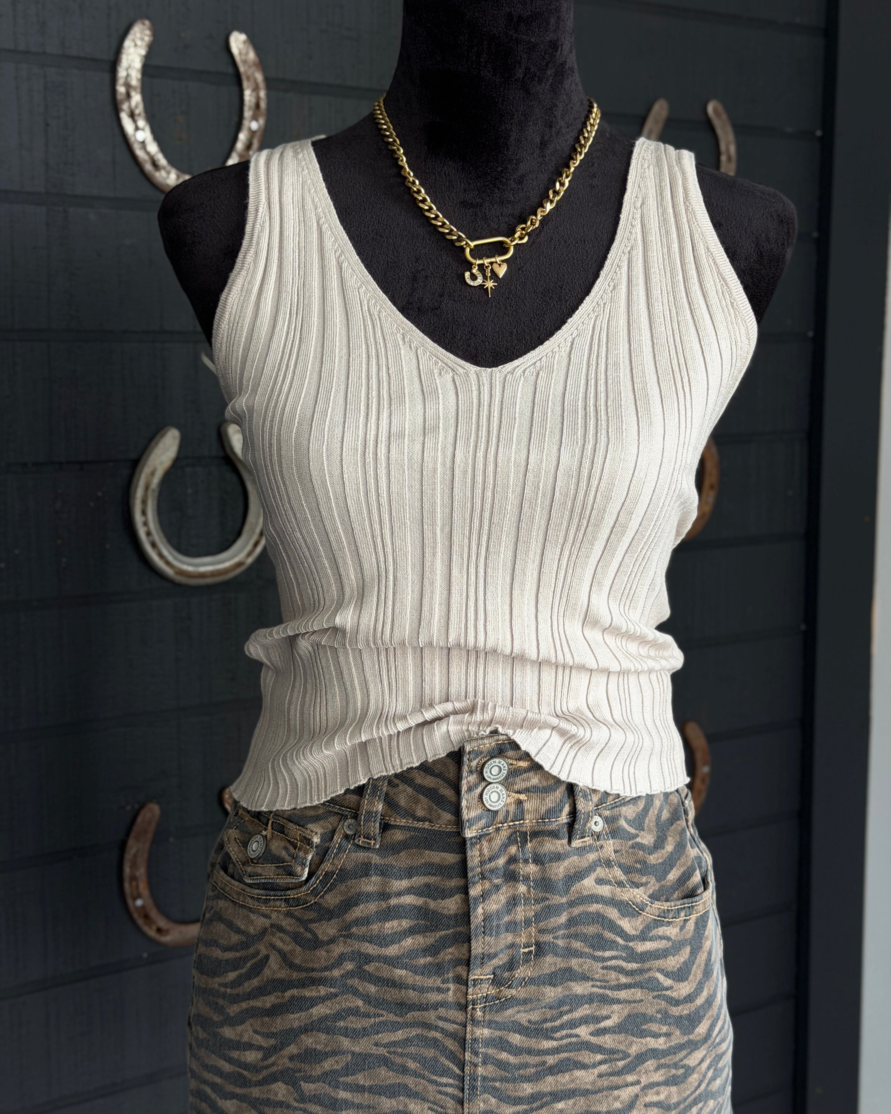 Mannequin wearing a white ribbed tank top and patterned pants with gold jewelry against a dark background.
