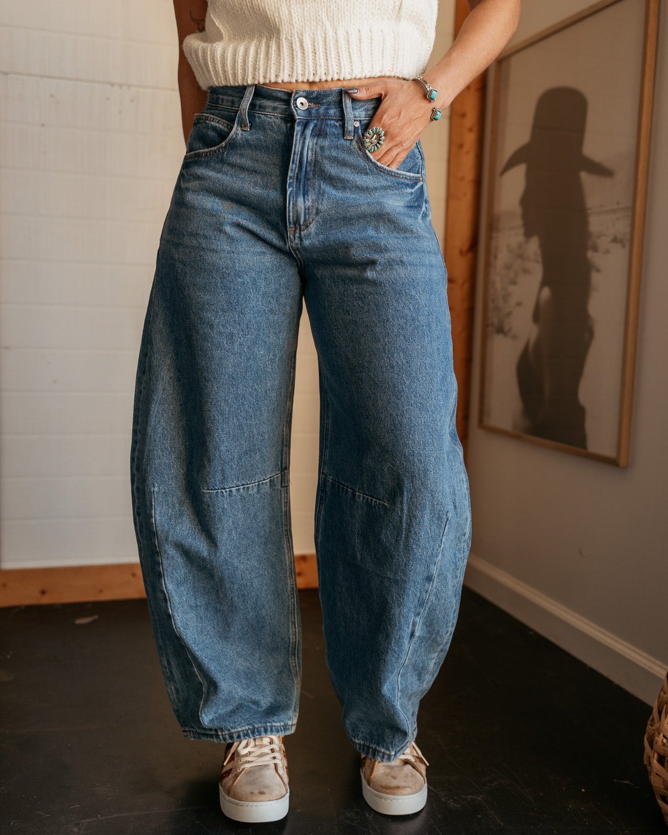 Woman wearing wide leg denim jeans, cream knit crop top, western jewelry, and sneakers
