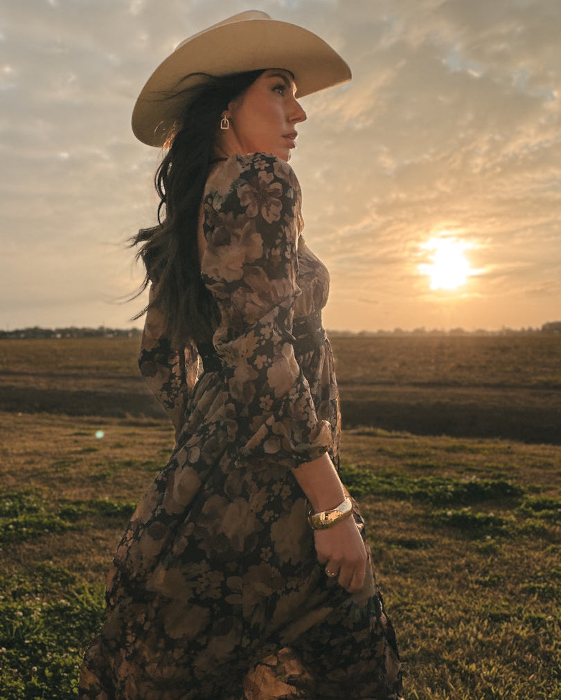 Woman in floral western dress and cowboy hat at sunset in a boho country field