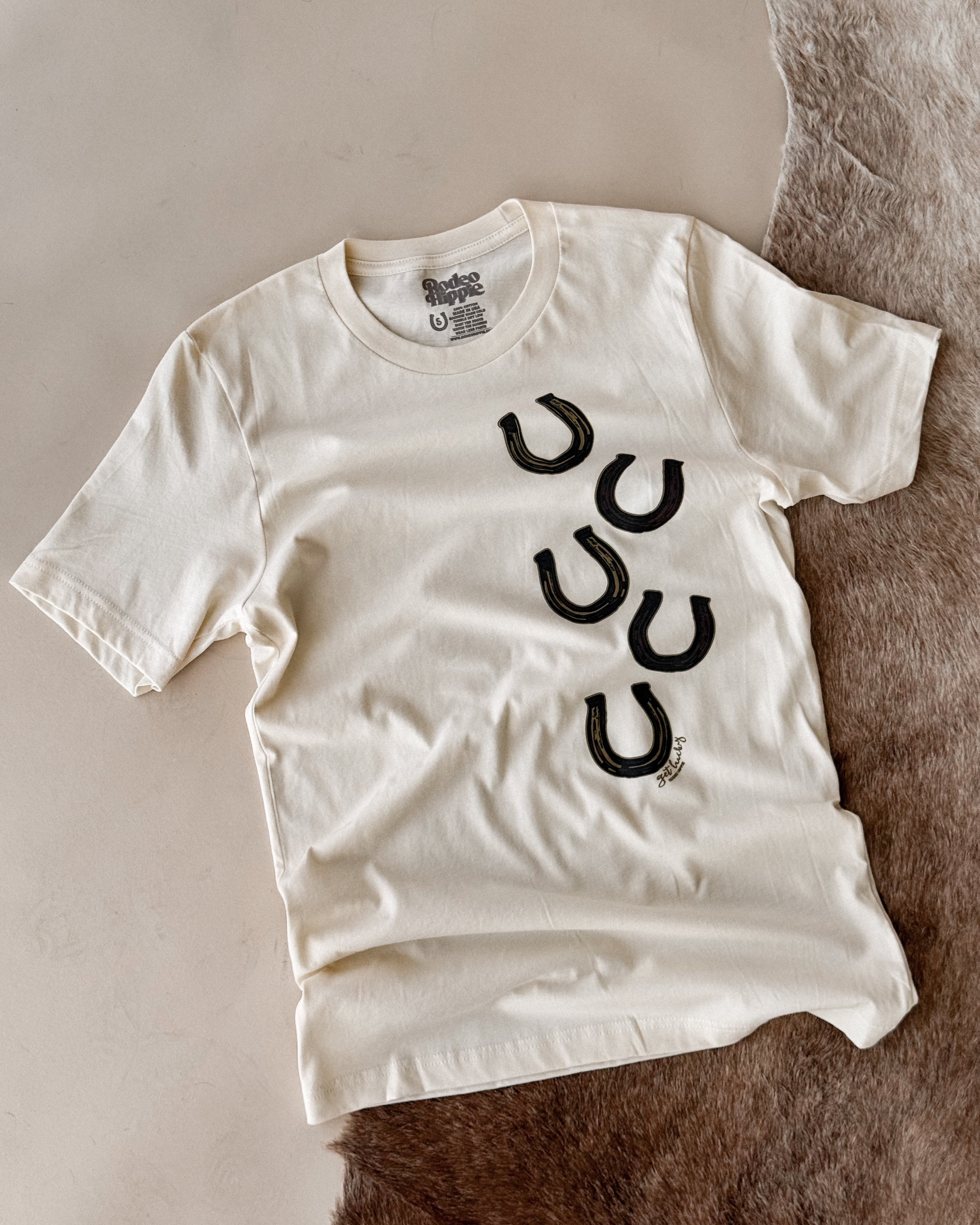 Western graphic tee with black horseshoe prints, laid on a fur rug, cowgirl boho outfit