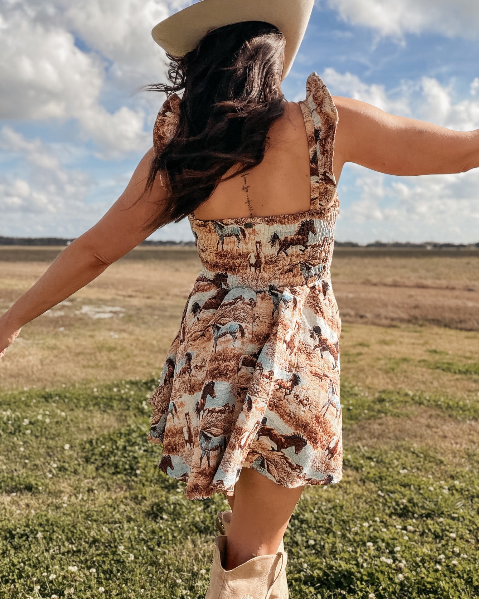 Woman in a cowboy hat and western horse print dress with boots in an open field