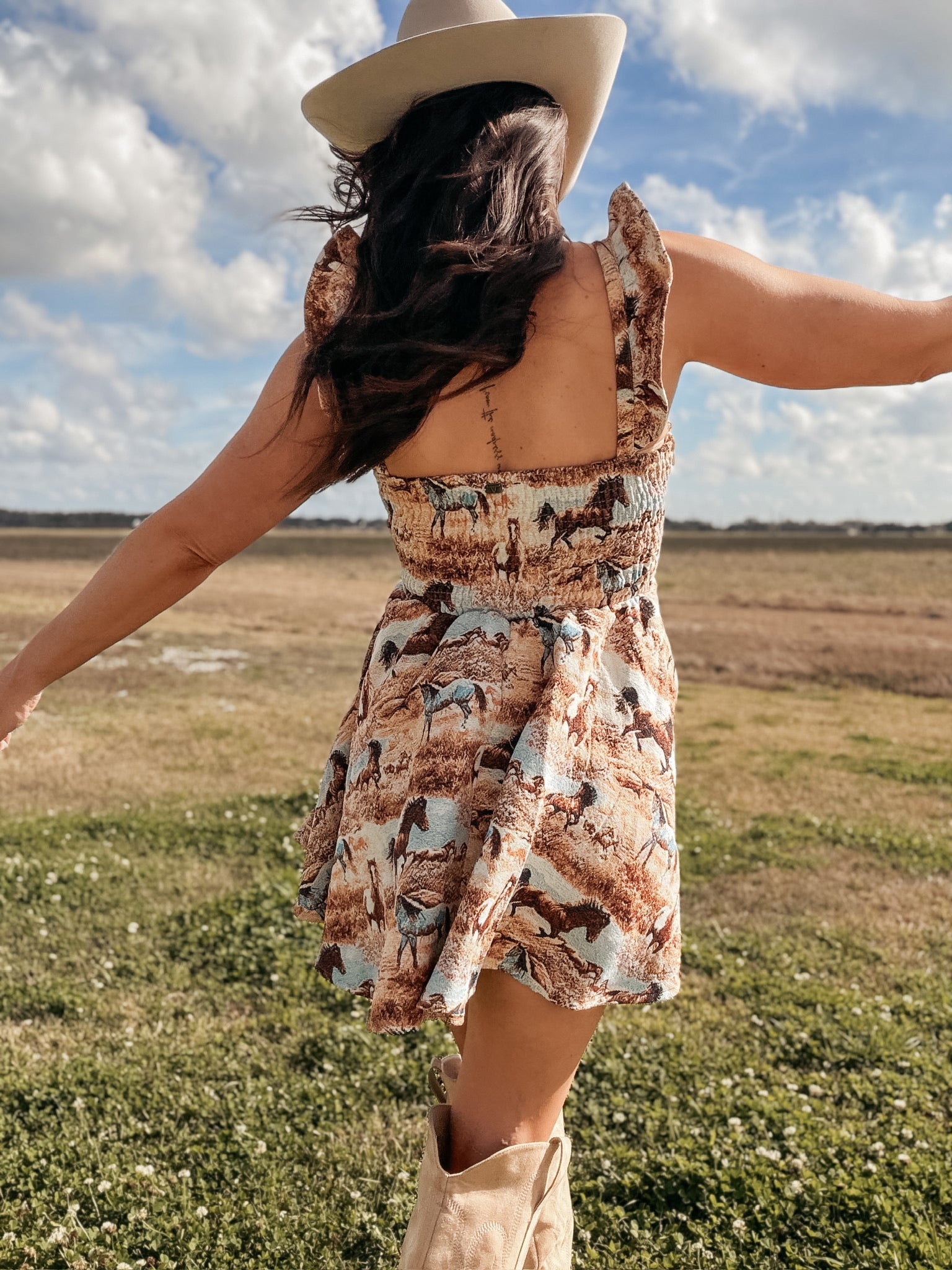 Woman in a cowboy hat and western horse print dress with boots in an open field