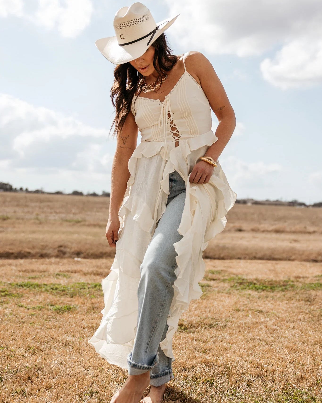 Woman in a white cowboy hat, ruffled boho western dress and blue jeans outdoors