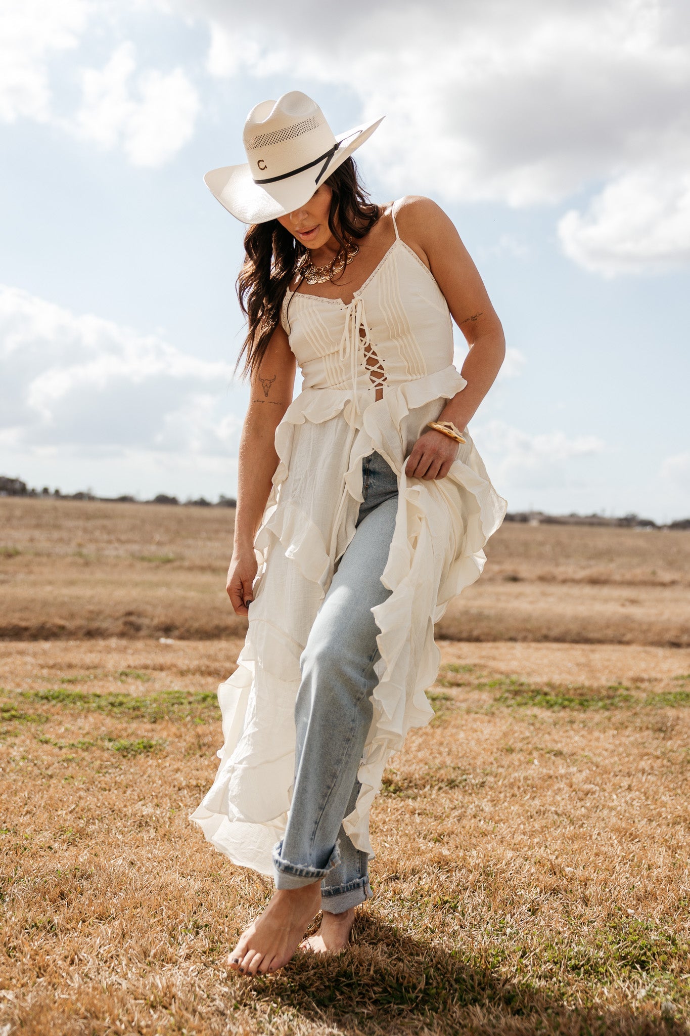 Woman in a white cowboy hat, ruffled boho western dress and blue jeans outdoors