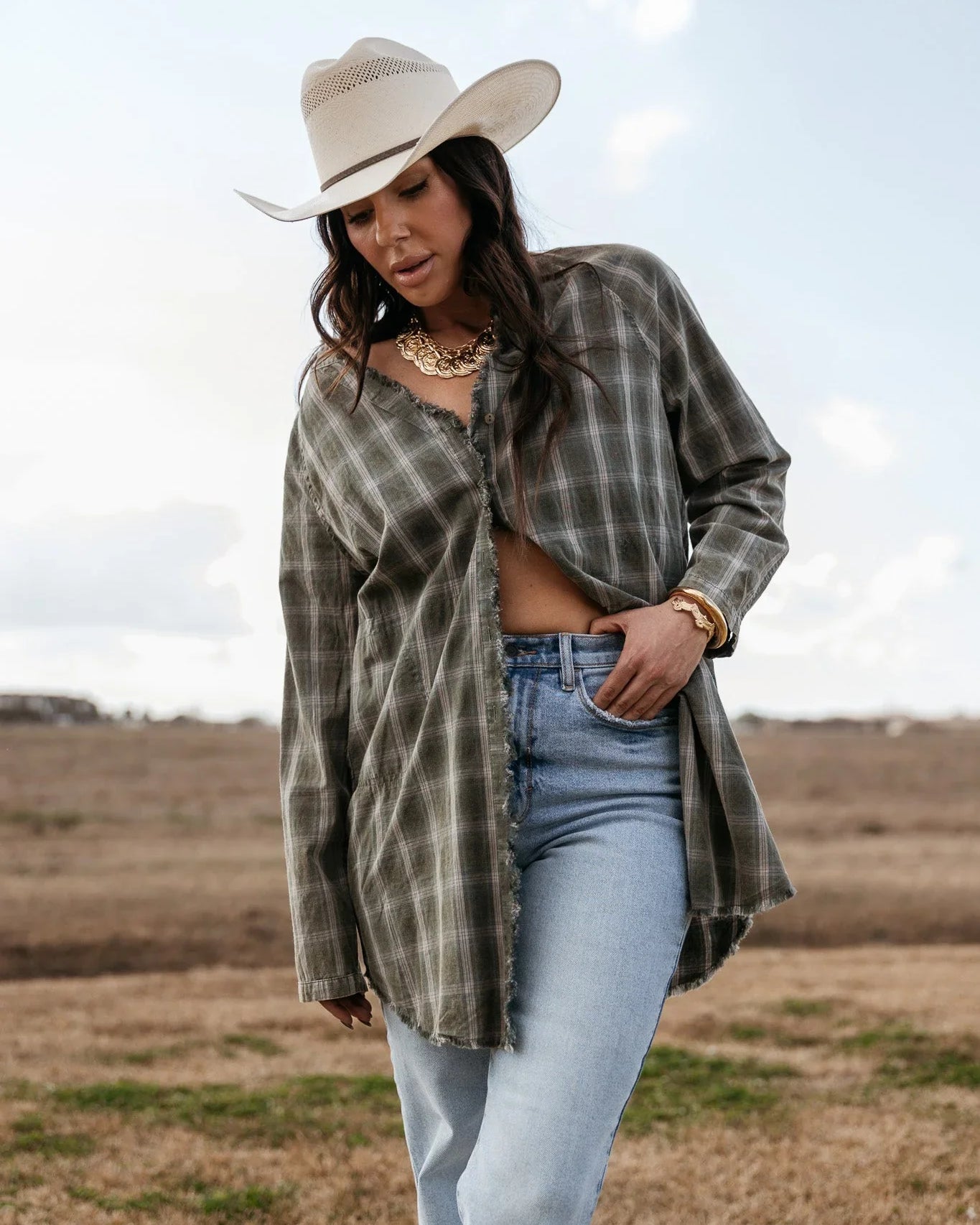 Woman in a white cowboy hat, plaid shirt, and light wash jeans in a western field setting