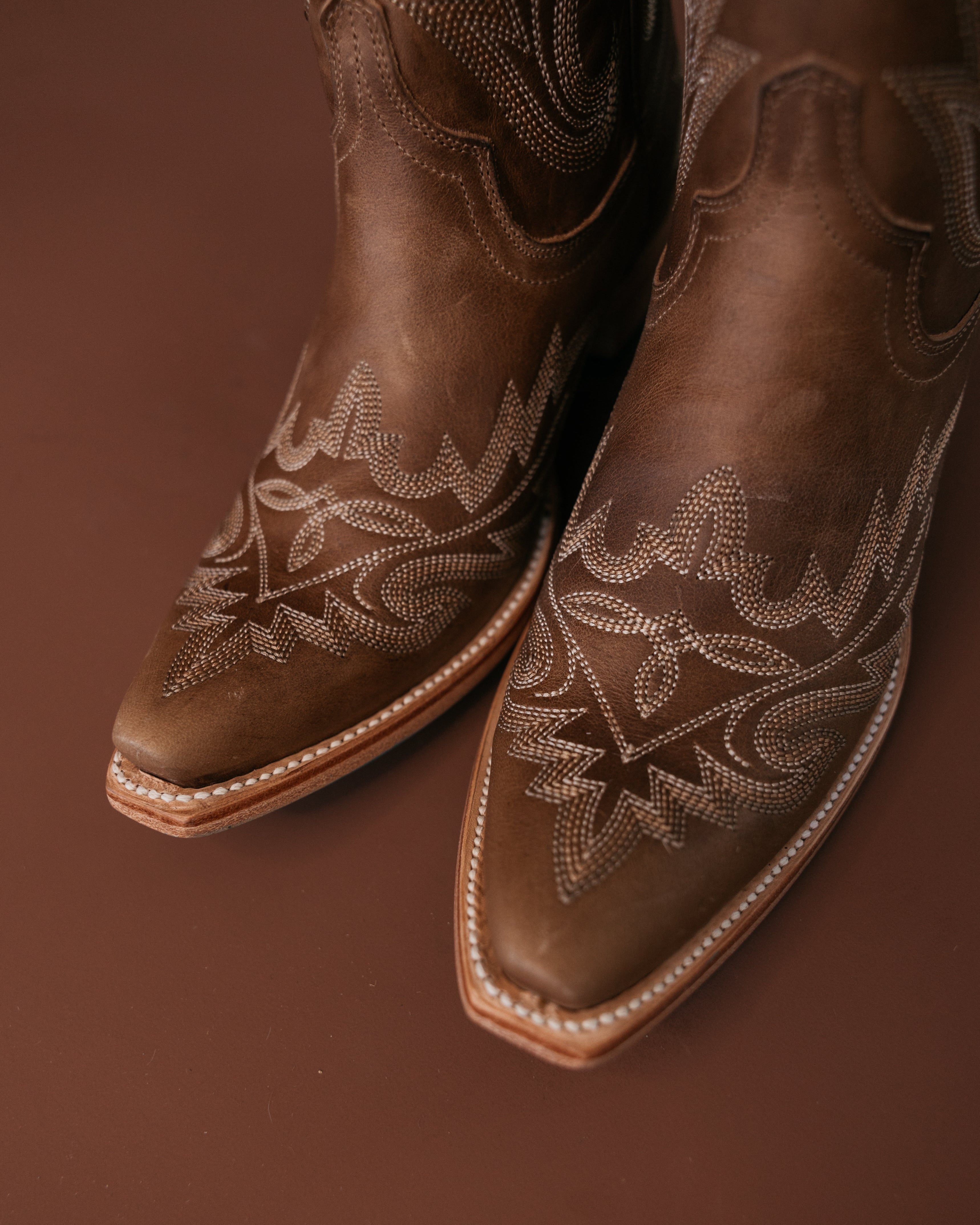 Brown leather western cowgirl boots with intricate white stitching on pointed toes