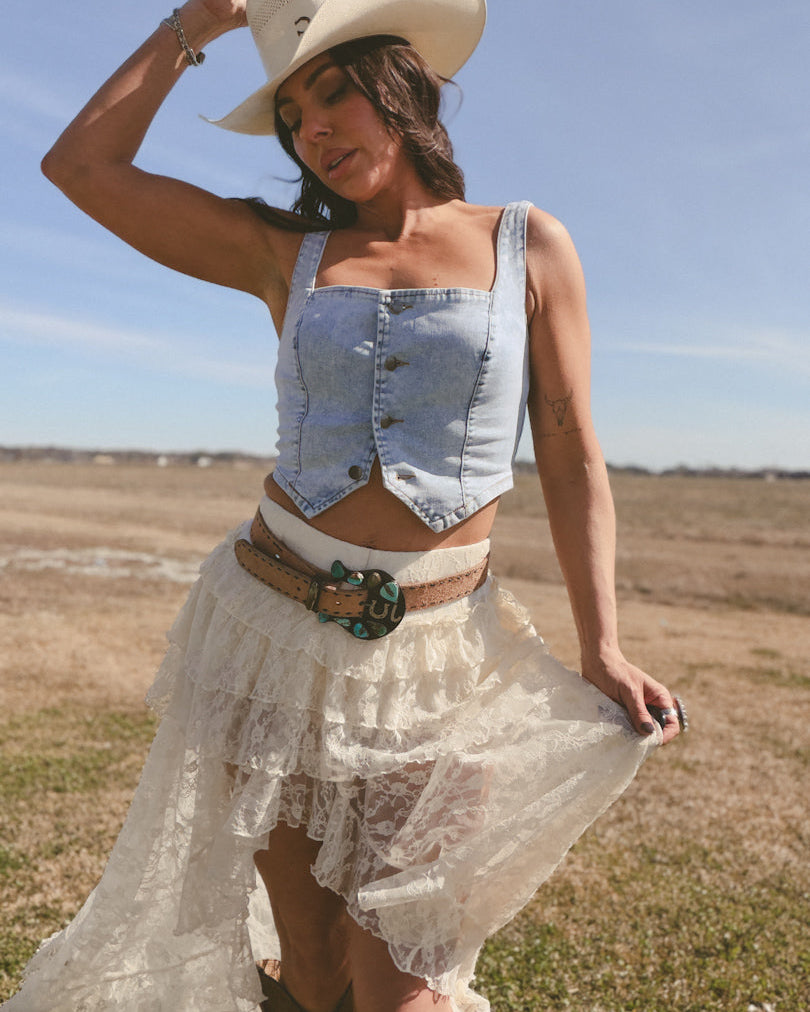 Woman in cowgirl hat, denim crop top, and lace skirt posing outdoors in western boho outfit