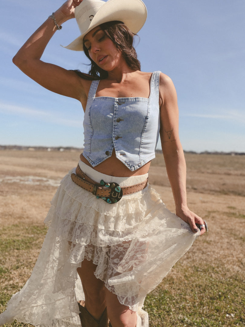 Woman in cowgirl hat, denim crop top, and lace skirt posing outdoors in western boho outfit