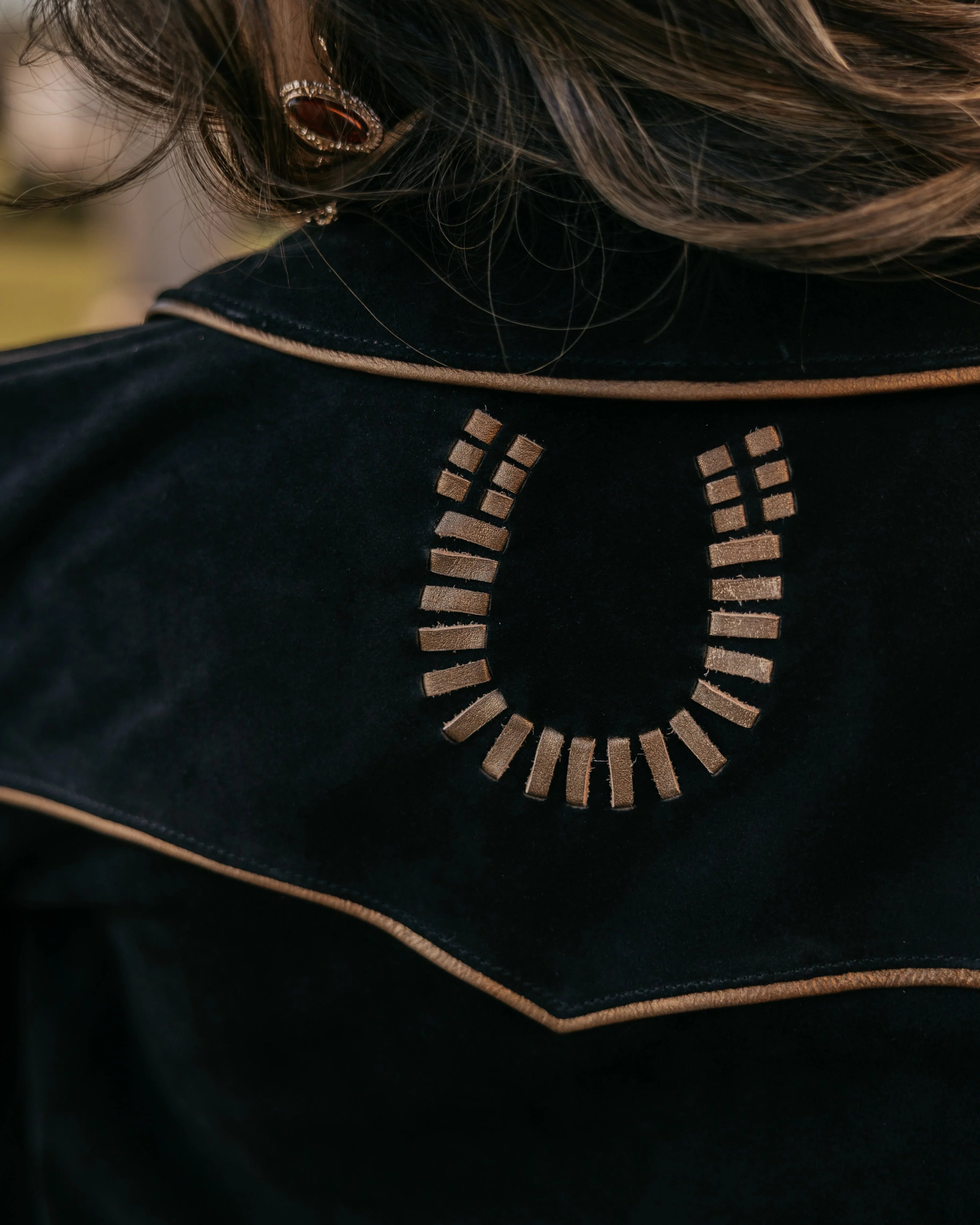 Close-up of western suede jacket with embroidered horseshoe design and brown piping
