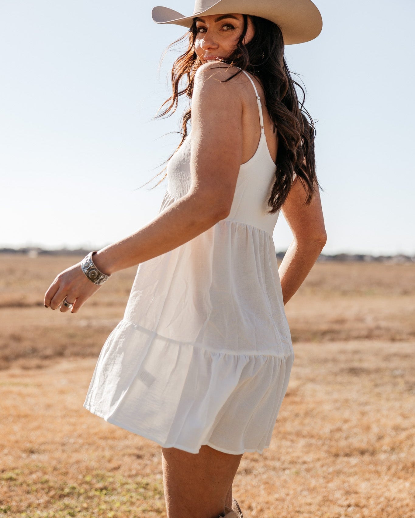 Woman in a white western dress, cowboy hat, and boots outdoors in a boho cowgirl style.