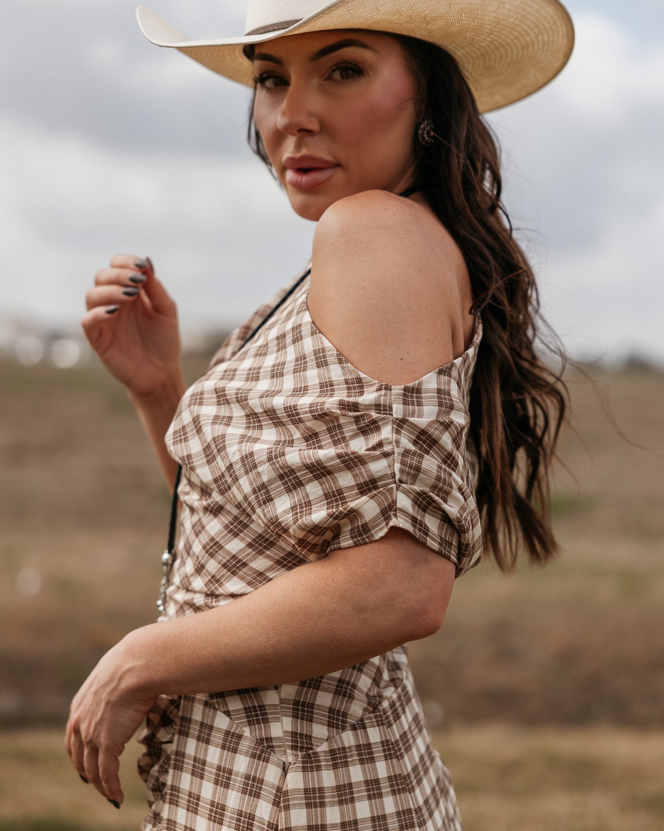 Woman in western plaid off-shoulder dress and cowboy hat outdoors, cowgirl boho style