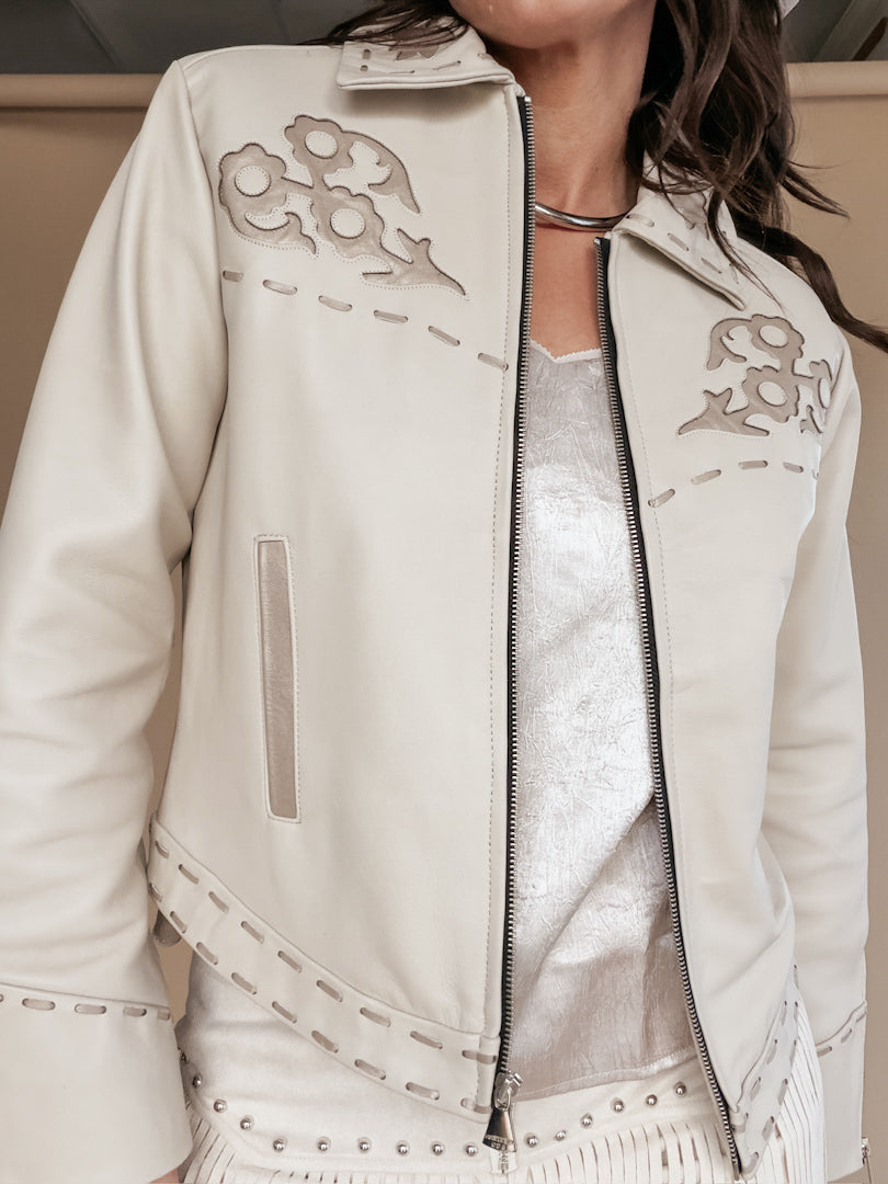 Woman wearing a cream western jacket with floral cutout details and a silver necklace