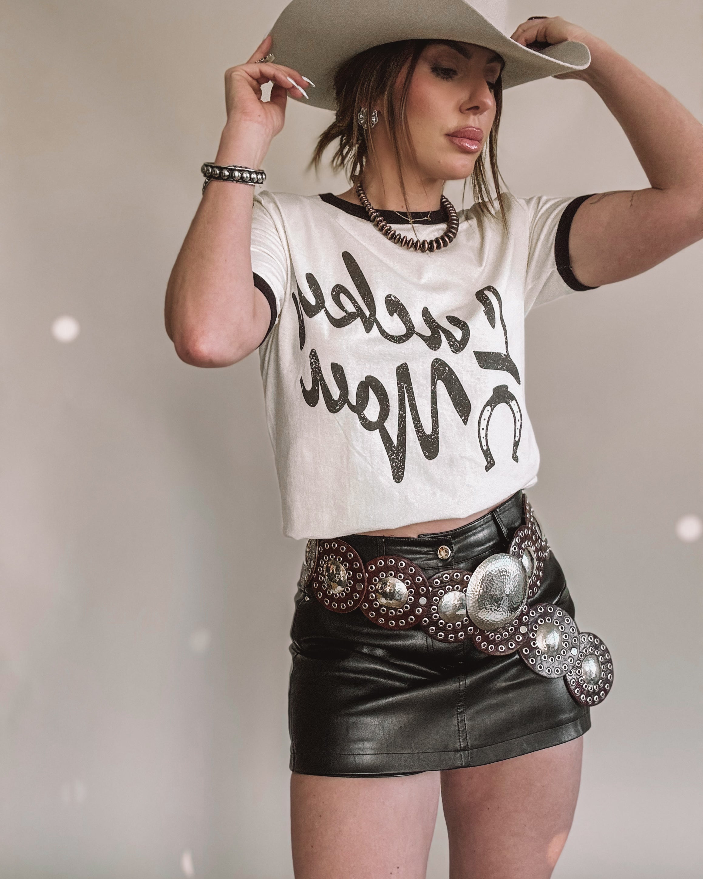 Woman in western boho outfit with cowboy hat, graphic tee, leather mini skirt and concho belt