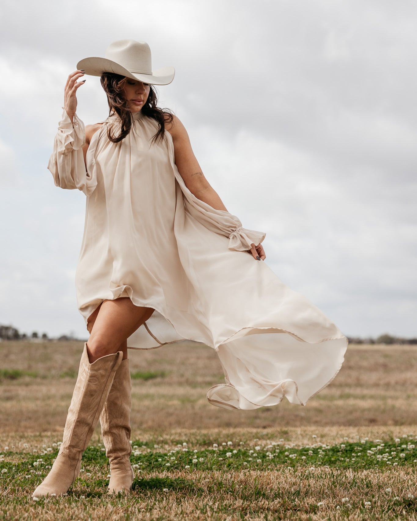 Woman in cream western boho dress and cowboy hat with suede boots in a field