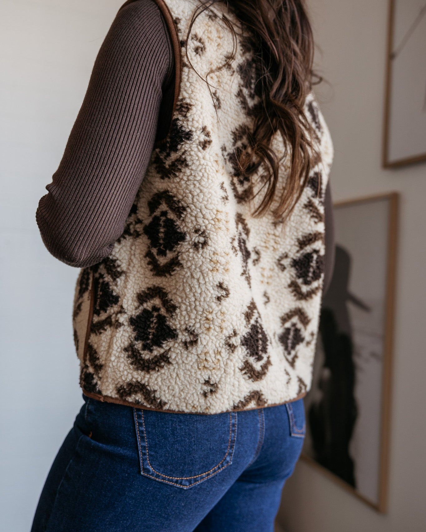 Woman wearing sherpa western print vest, ribbed brown top, and blue jeans