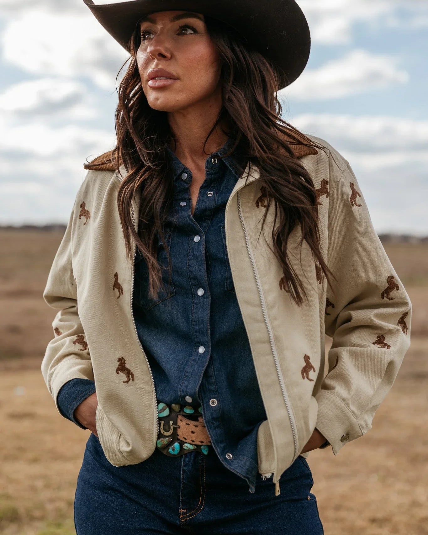 Woman in western denim outfit, embroidered jacket, brown cowgirl hat outdoors