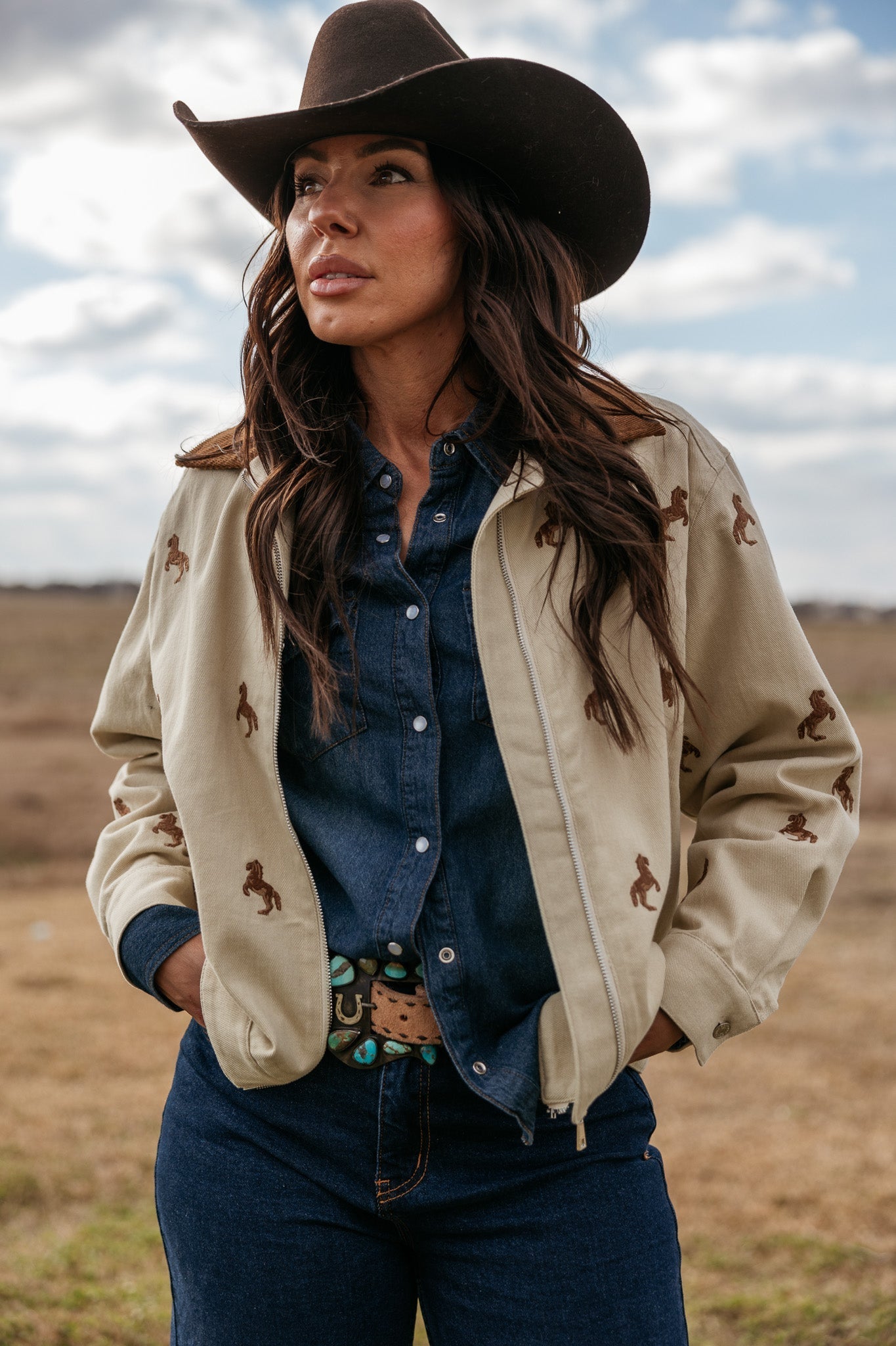 Woman in western denim outfit, embroidered jacket, brown cowgirl hat outdoors