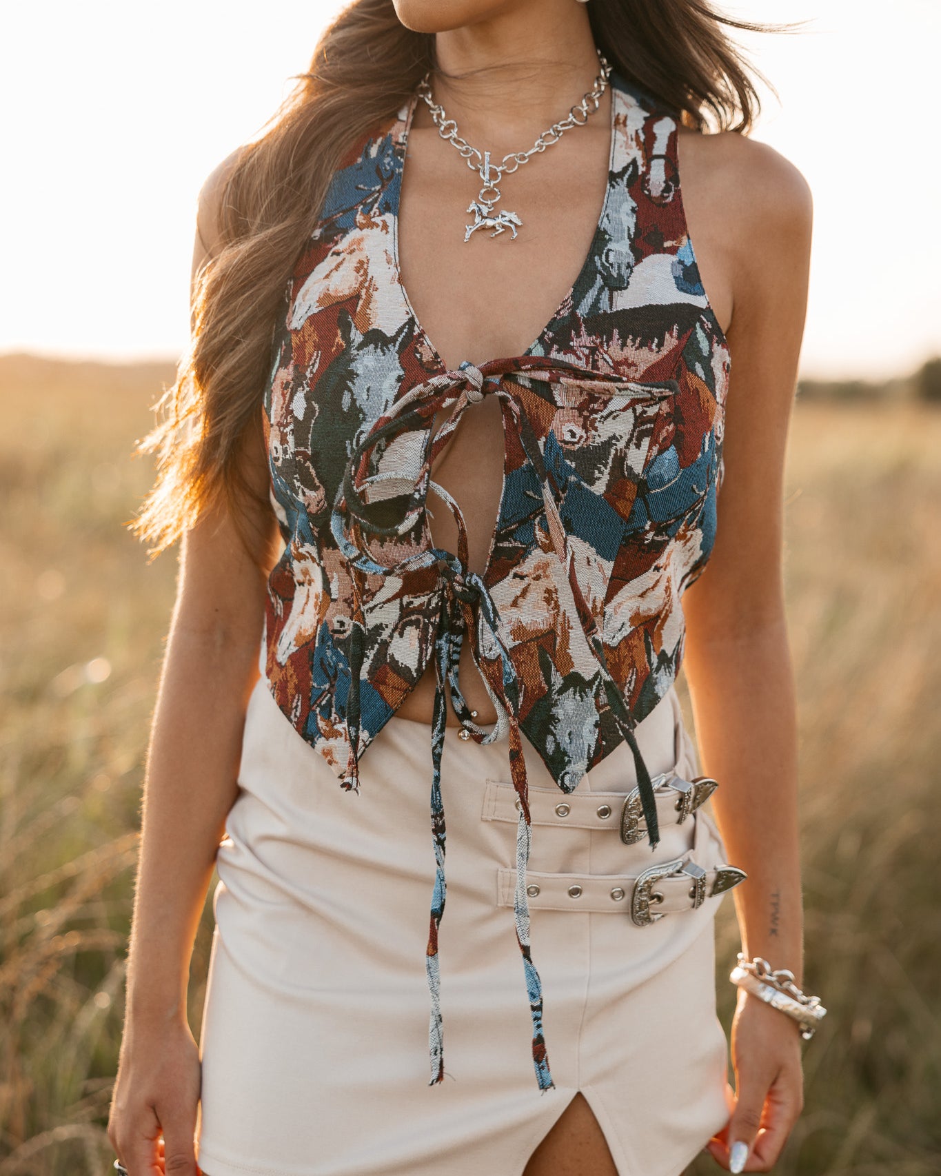 women wearing tie front halter top with horse pattern and a ivory skirt with buckles standing in a field.
