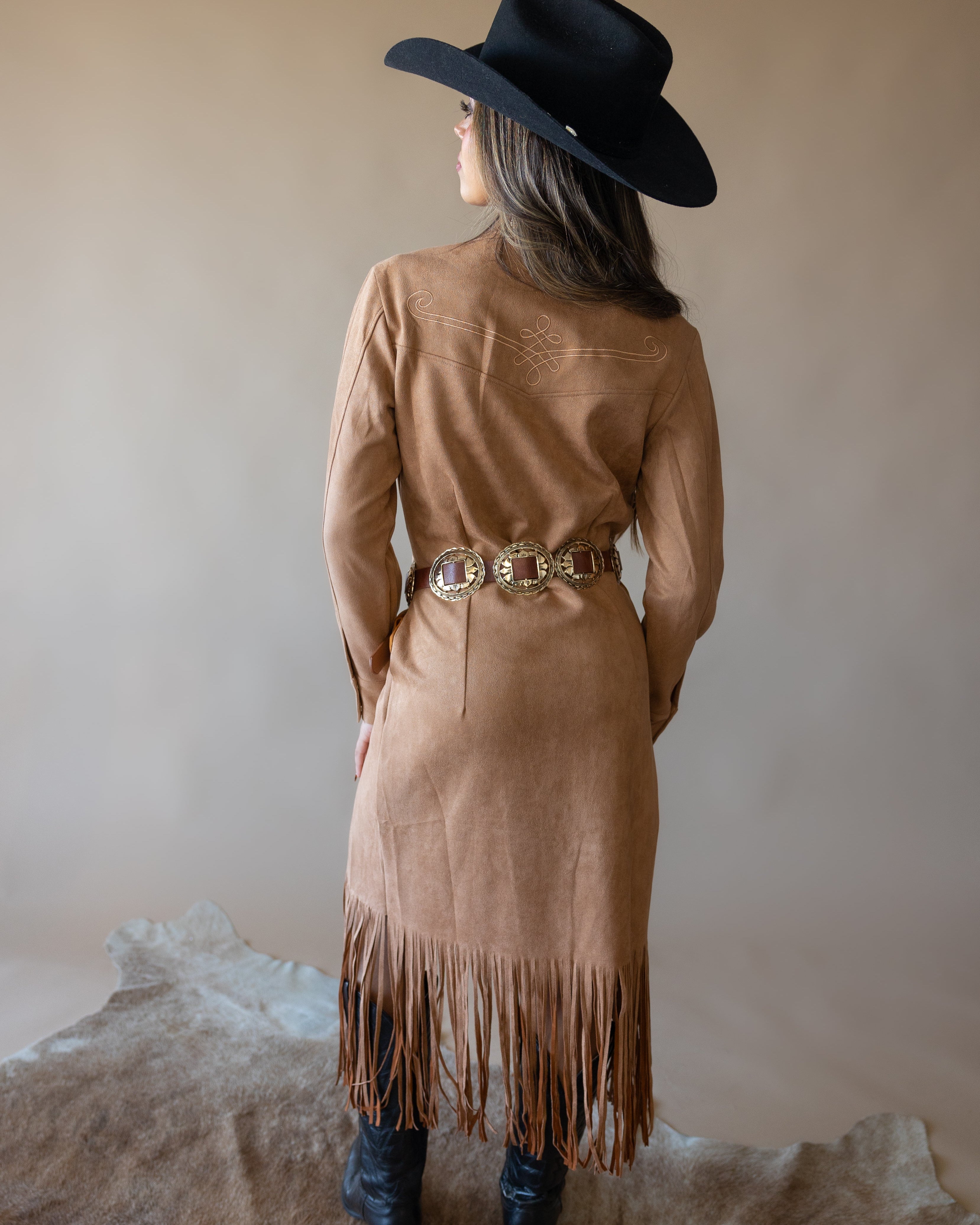 Woman in black cowboy hat, tan fringe suede western dress, and concho belt, back view