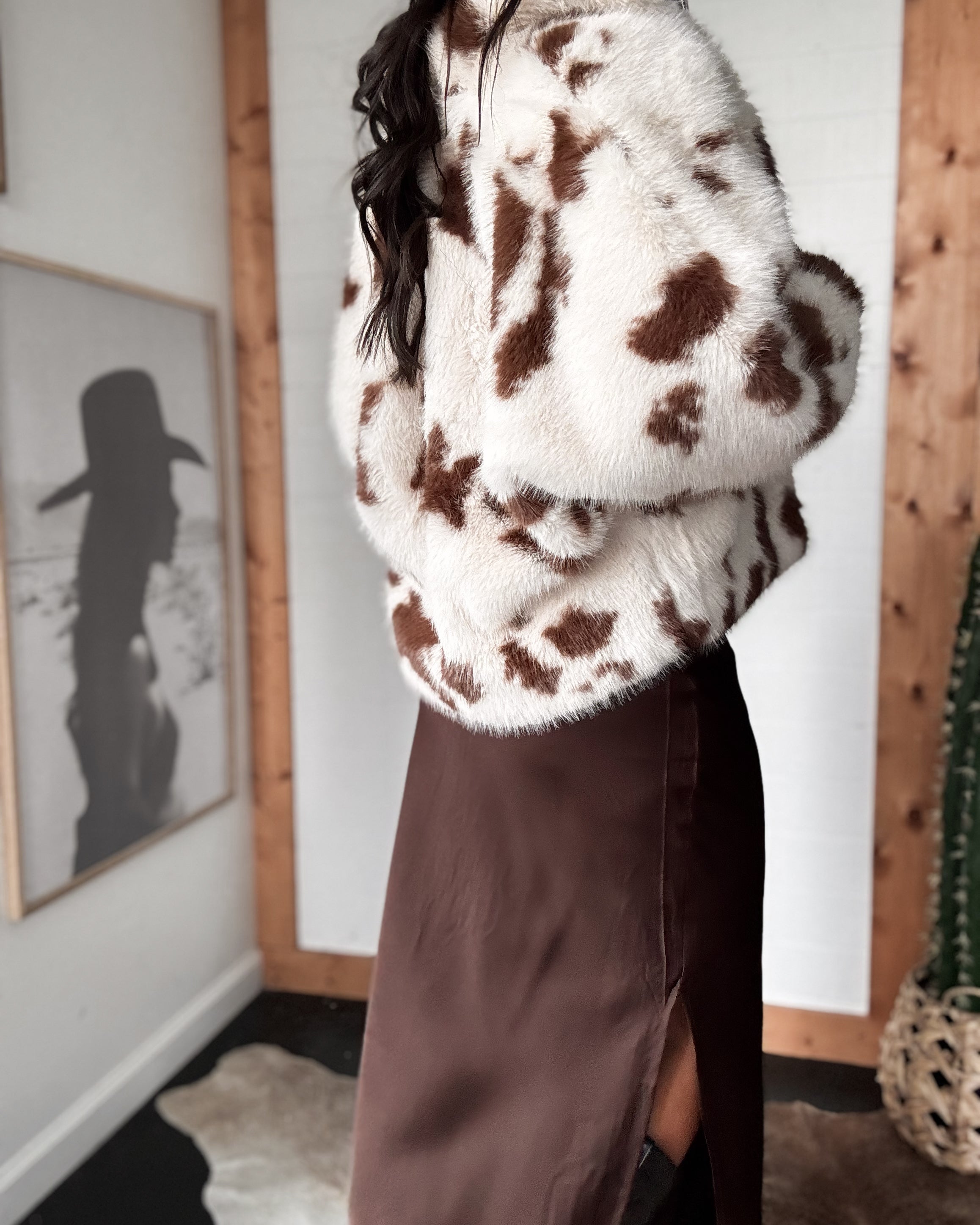 Person wearing a cow print sweater in a room with framed pictures on the wall.