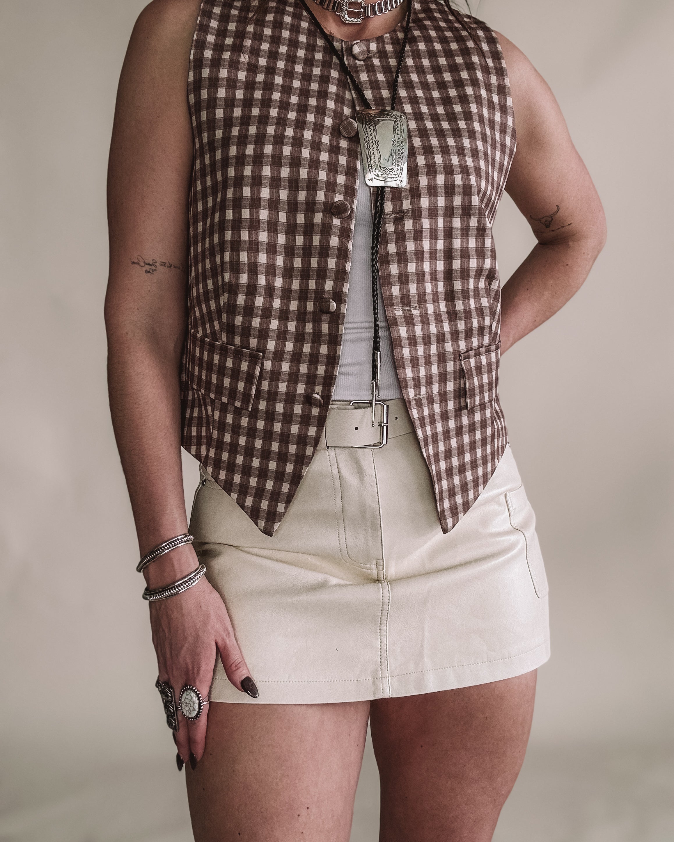 Woman in western boho outfit with brown checkered vest, leather mini skirt, and statement jewelry