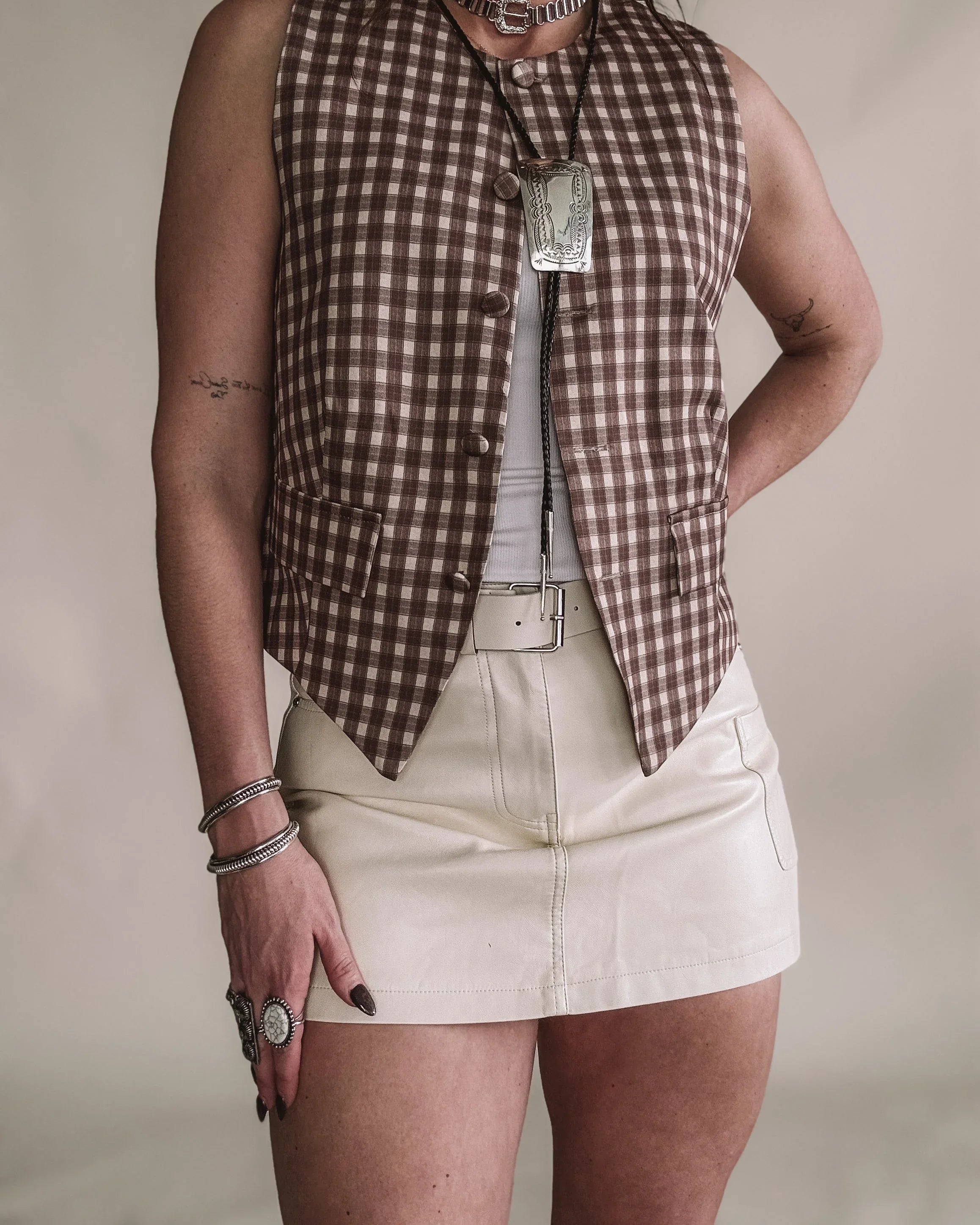 Woman in western boho outfit with brown checkered vest, leather mini skirt, and statement jewelry