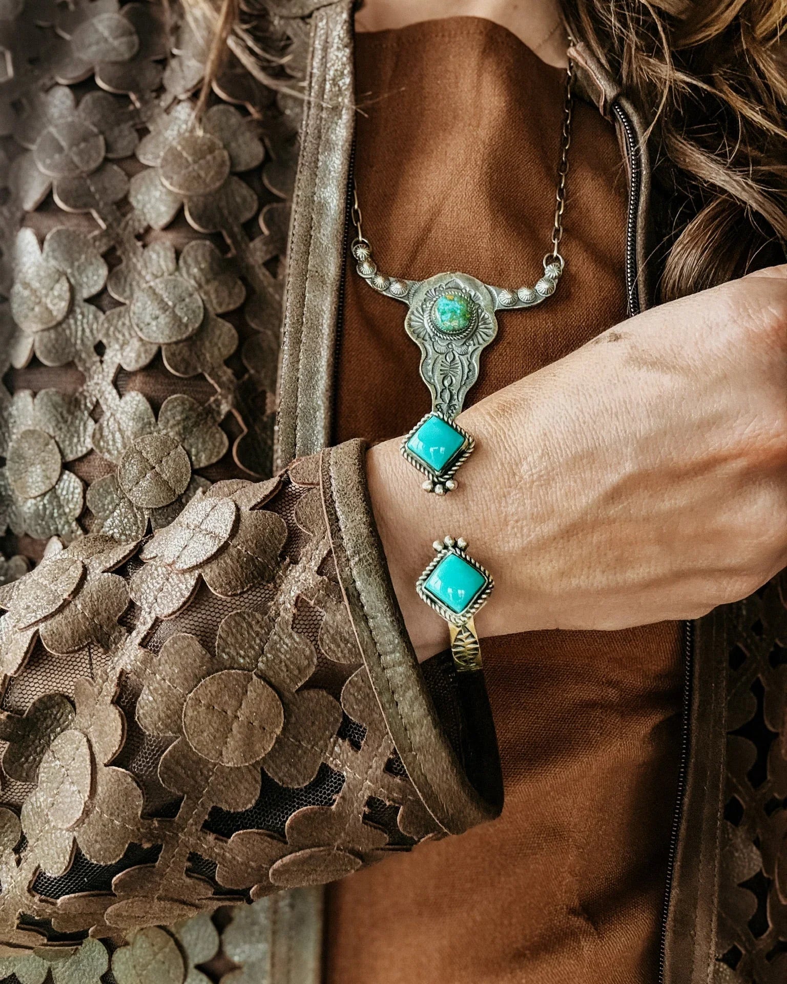 Person wearing turquoise jewelry with a textured brown bag