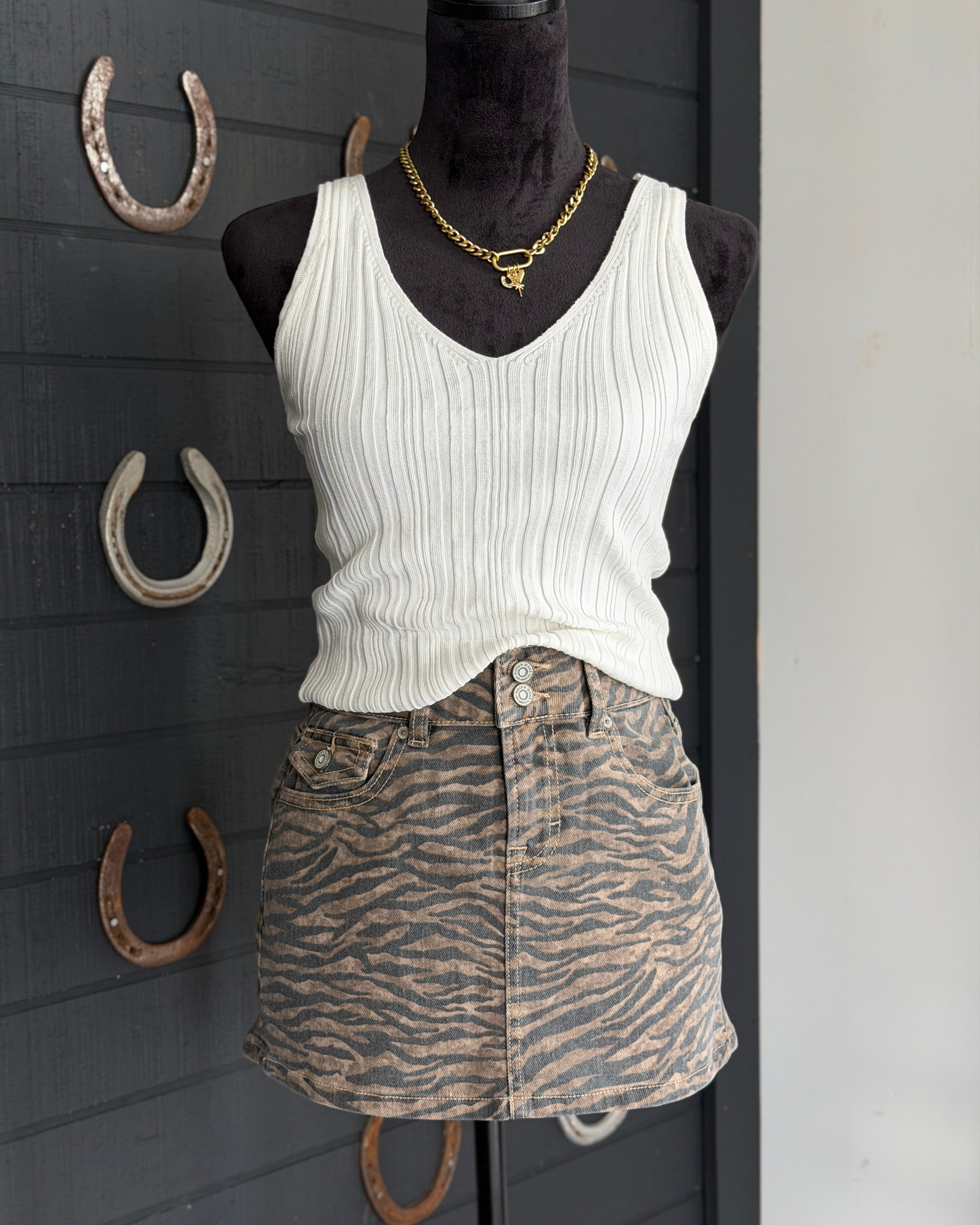 Mannequin wearing a white tank top and zebra print skirt with horseshoe decorations on a dark wall.