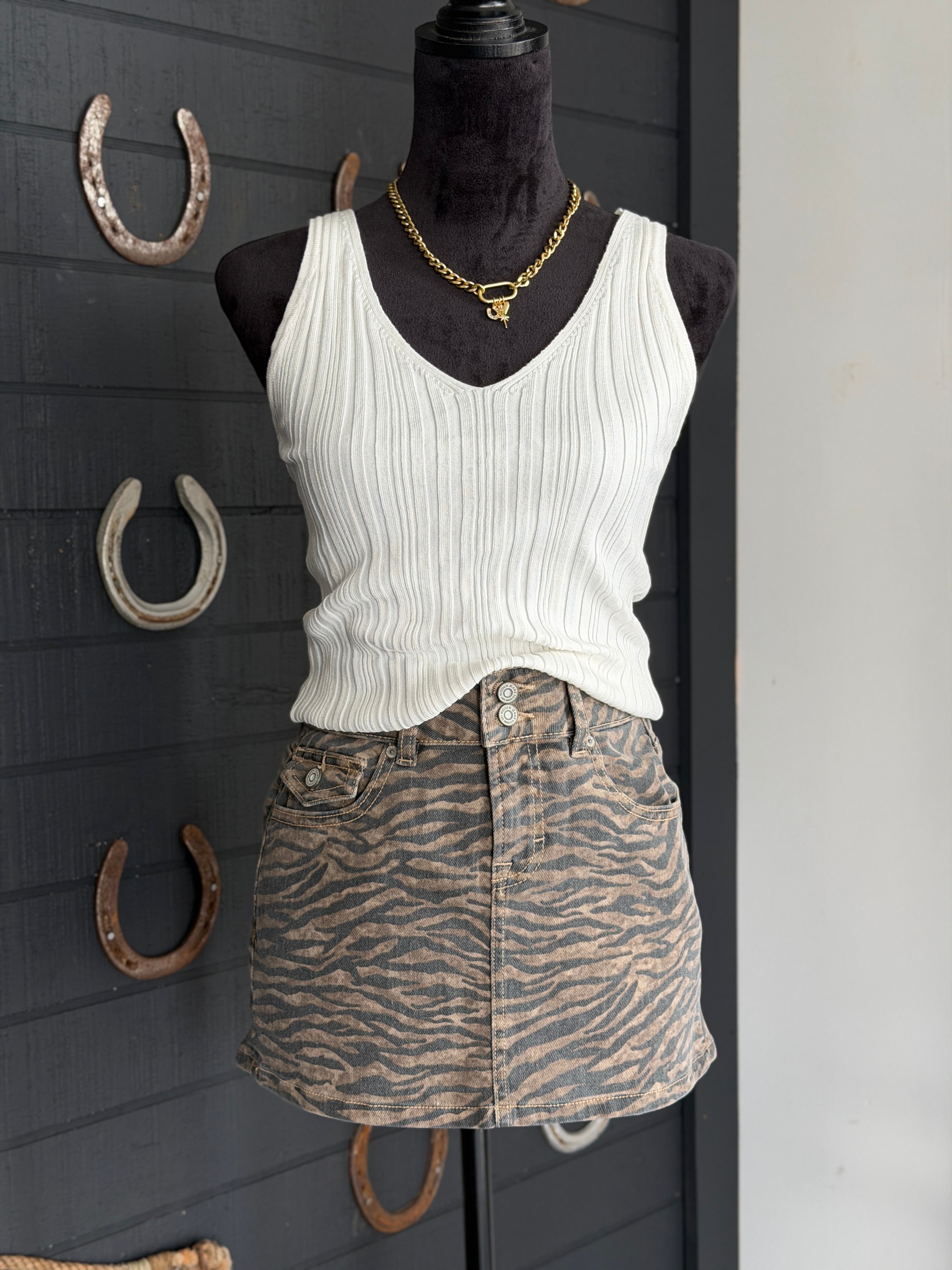Mannequin wearing a white tank top and zebra print skirt with horseshoe decorations on a dark wall.