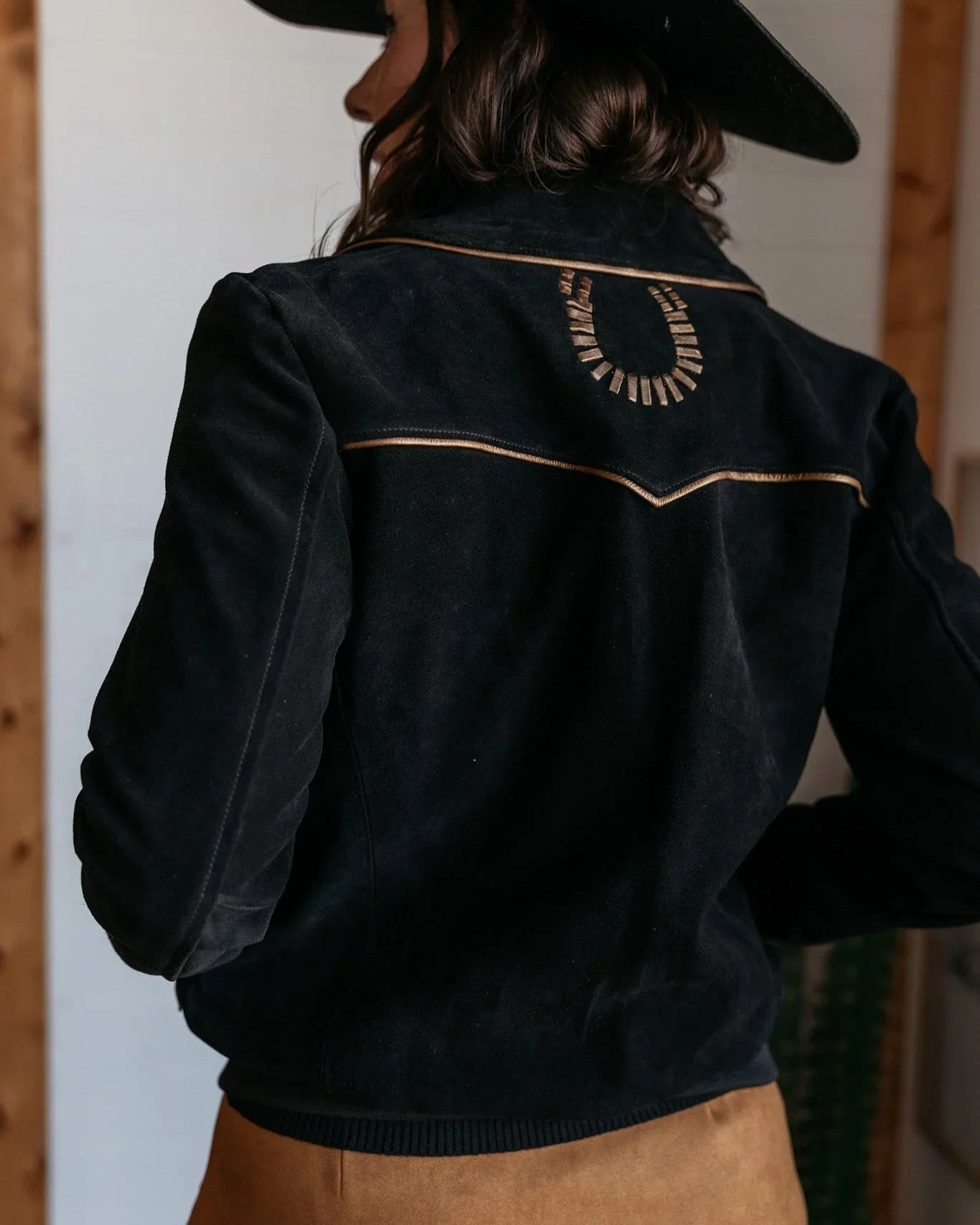 Woman in black western suede jacket with horseshoe detail and black cowboy hat