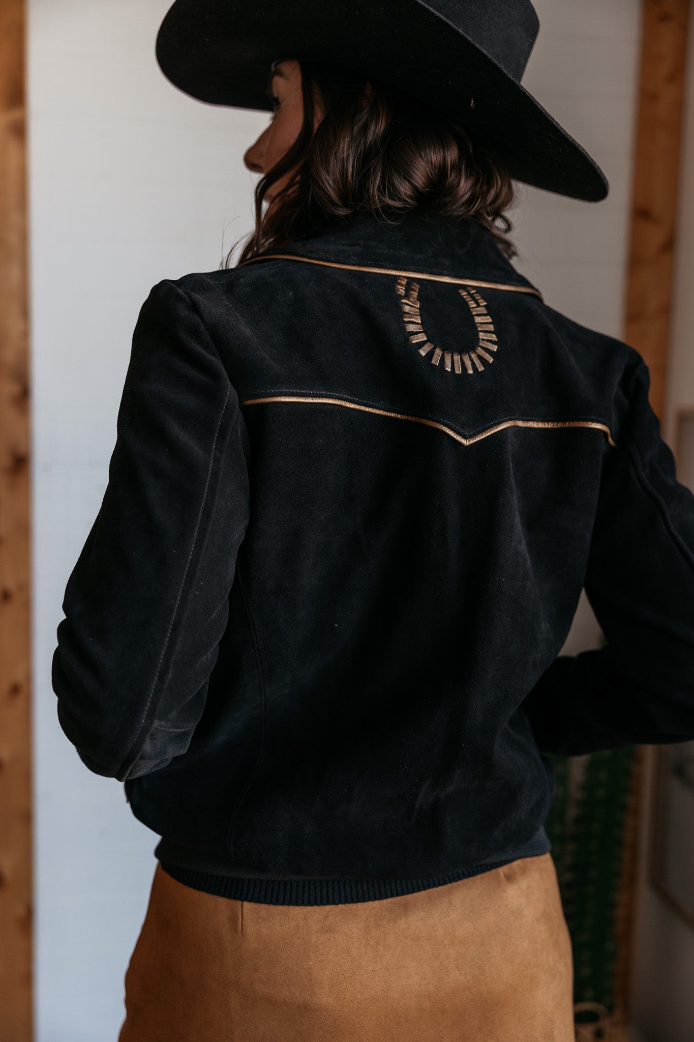 Woman in black western suede jacket with horseshoe detail and black cowboy hat