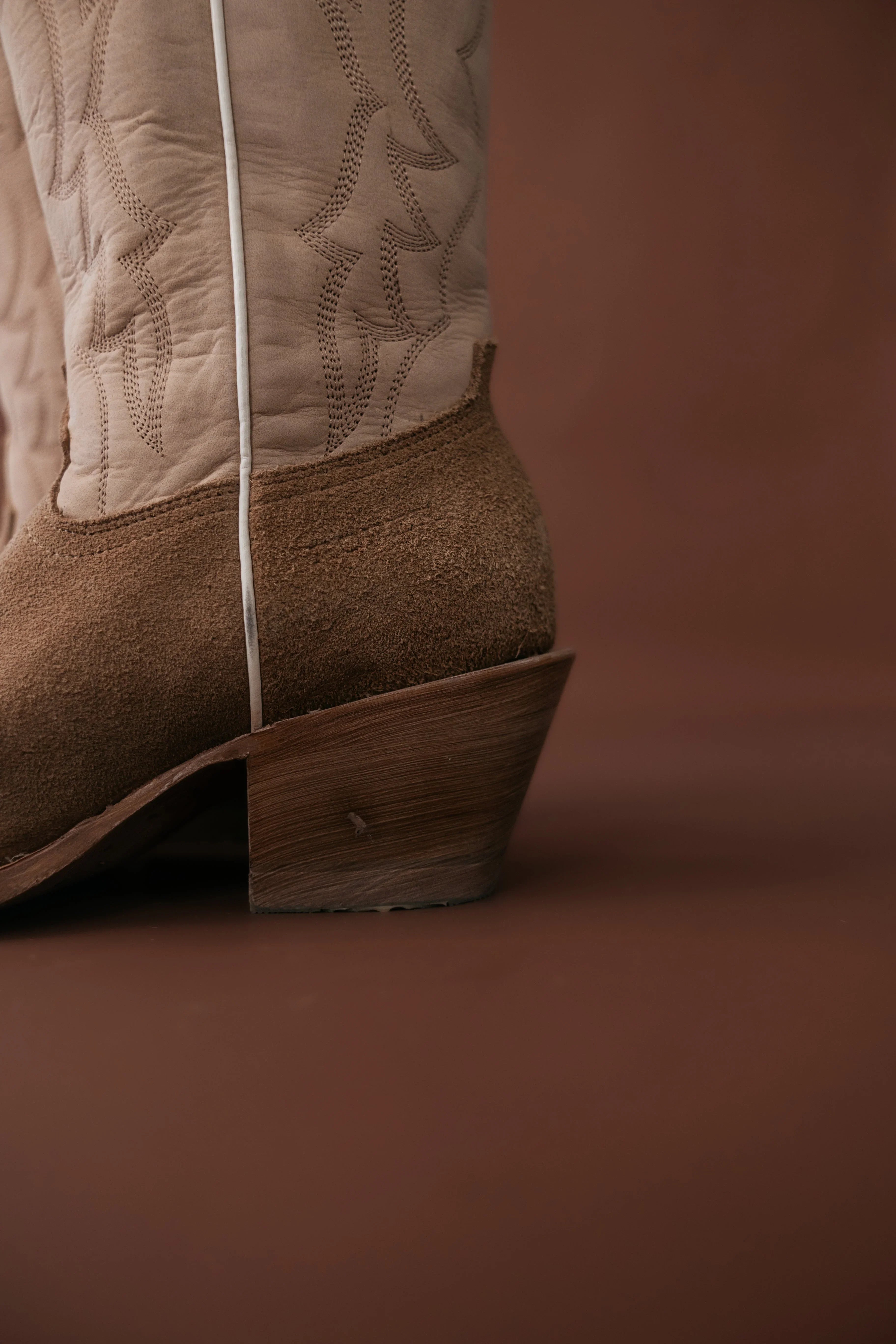 Close-up of a brown cowboy boot with detailed stitching on a brown background