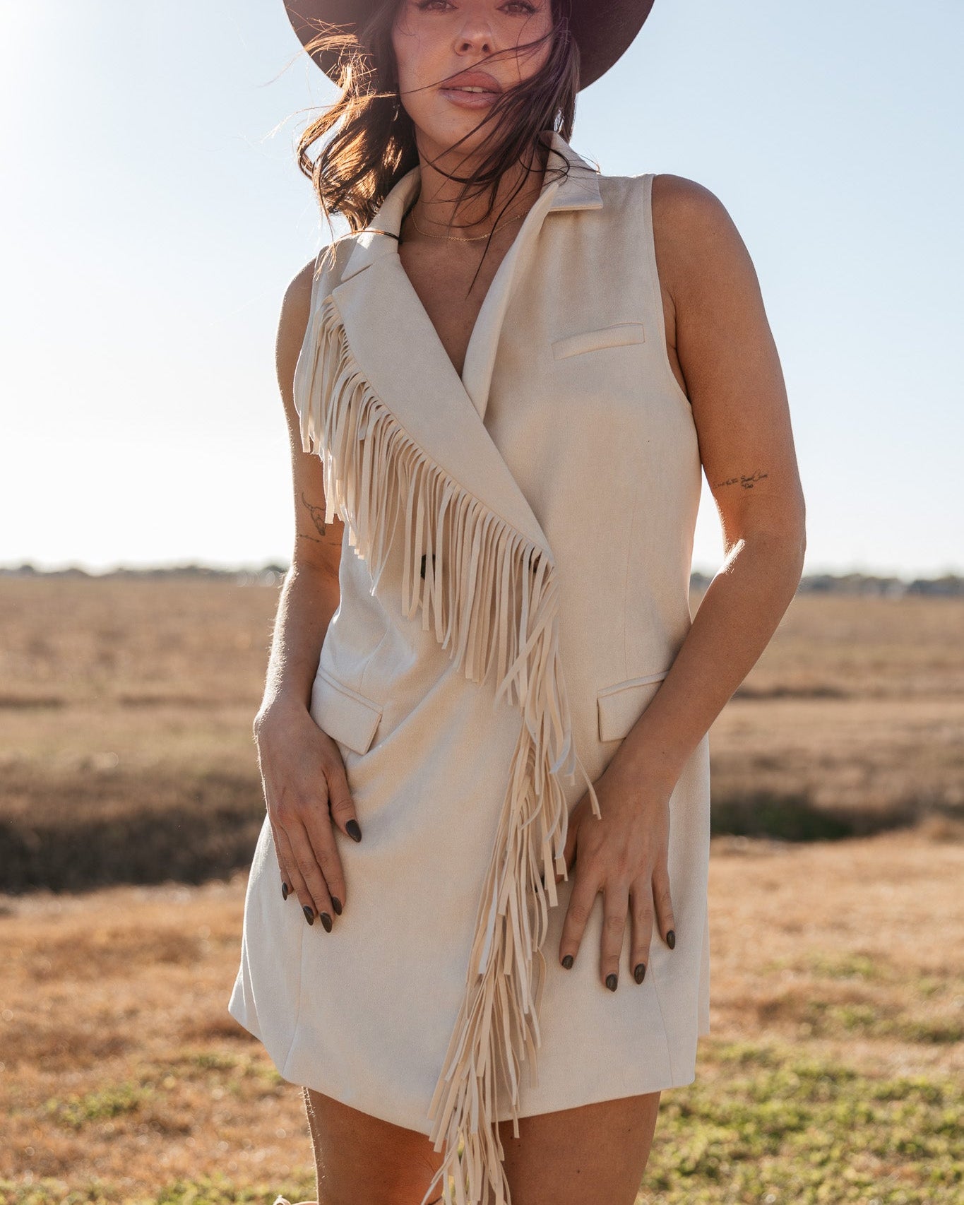Woman in cream fringe western vest dress and cowboy hat outdoors, cowgirl boho style